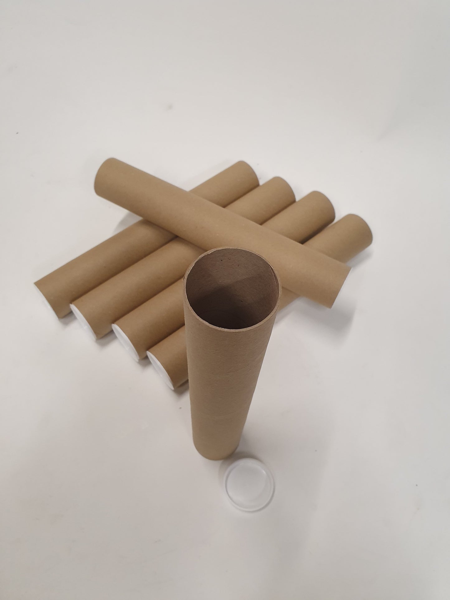 Top view of six brown cardboard packing tubes, one is positioned standing with the white plastic lid off.