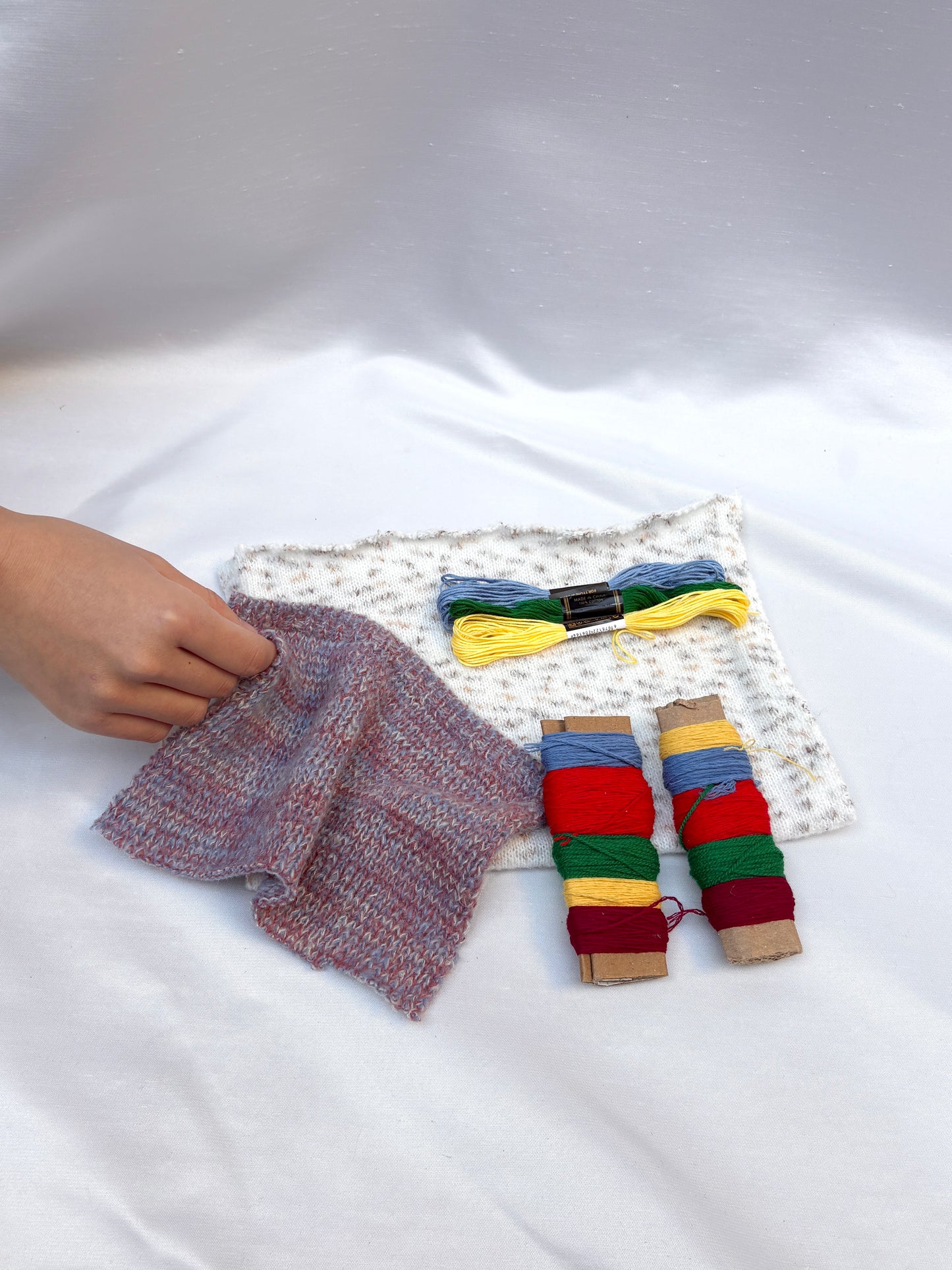 Hand holding textured fabric swatches with colourful thread and embroidery floss.