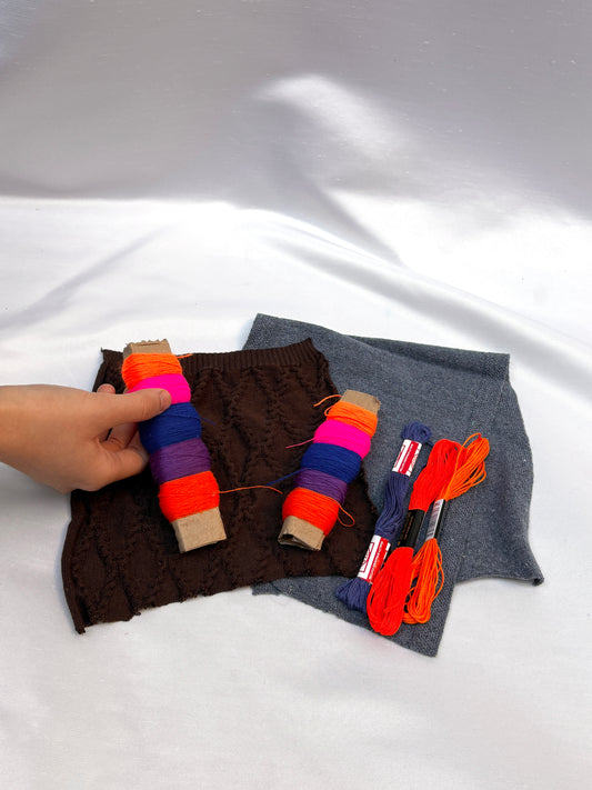 Hand holding fabric swatches with bright thread spools and embroidery floss.