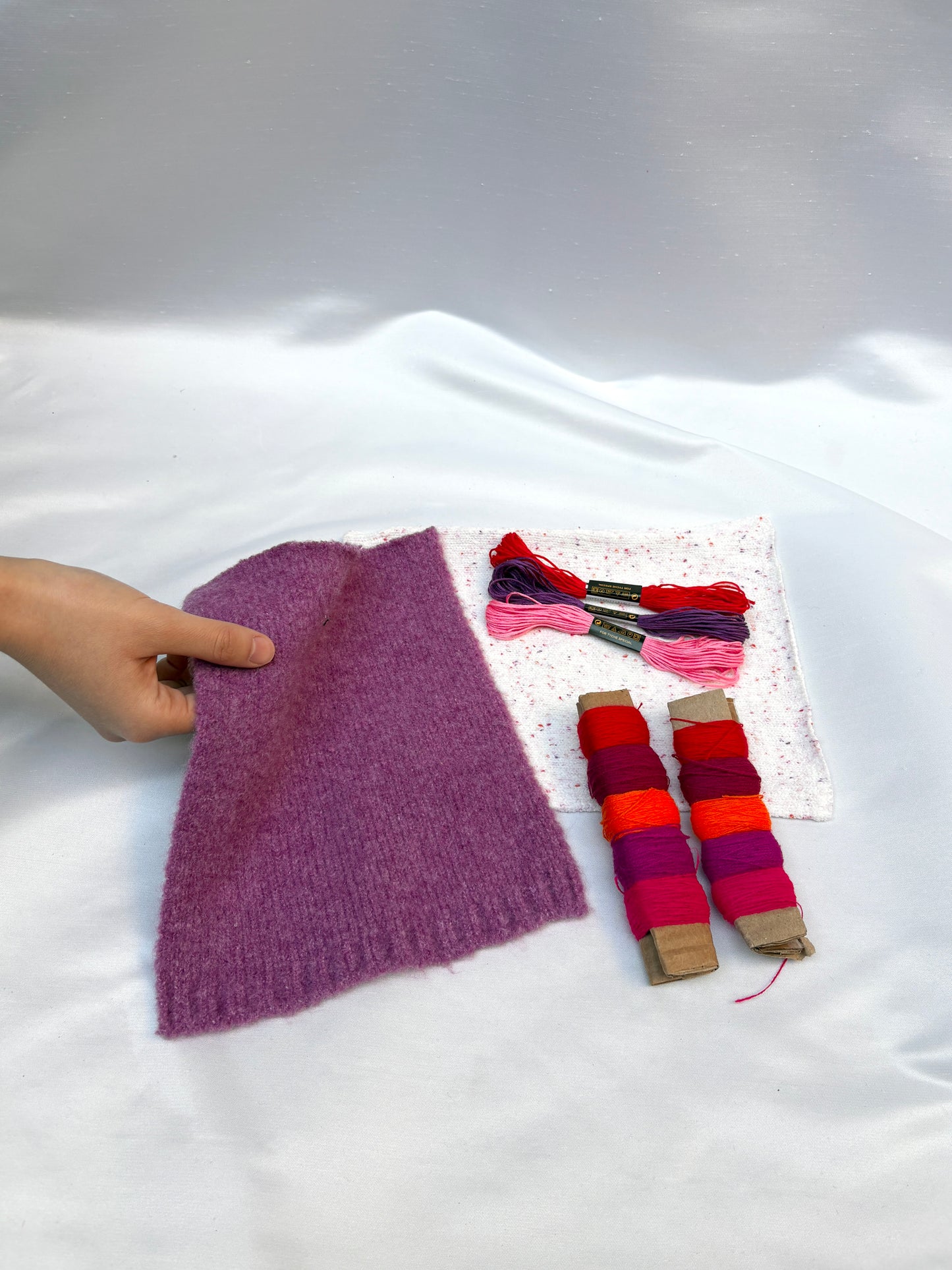 Hand holding soft fabric swatches with bright thread and embroidery floss.