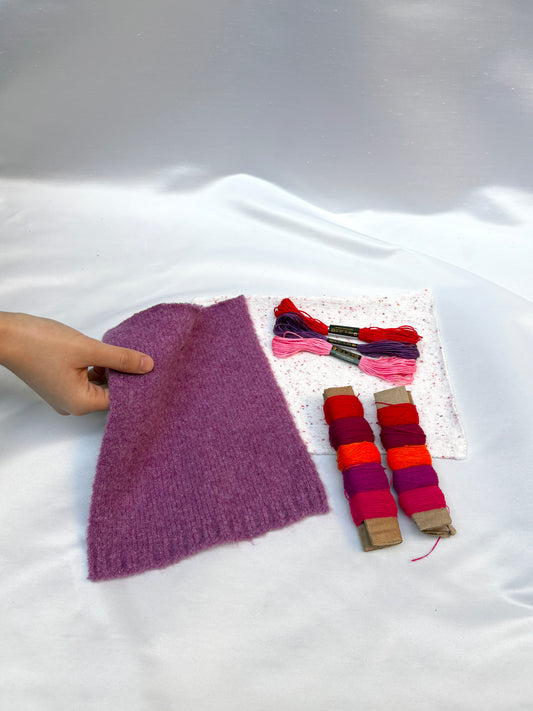 Hand holding soft fabric swatches with bright thread and embroidery floss.