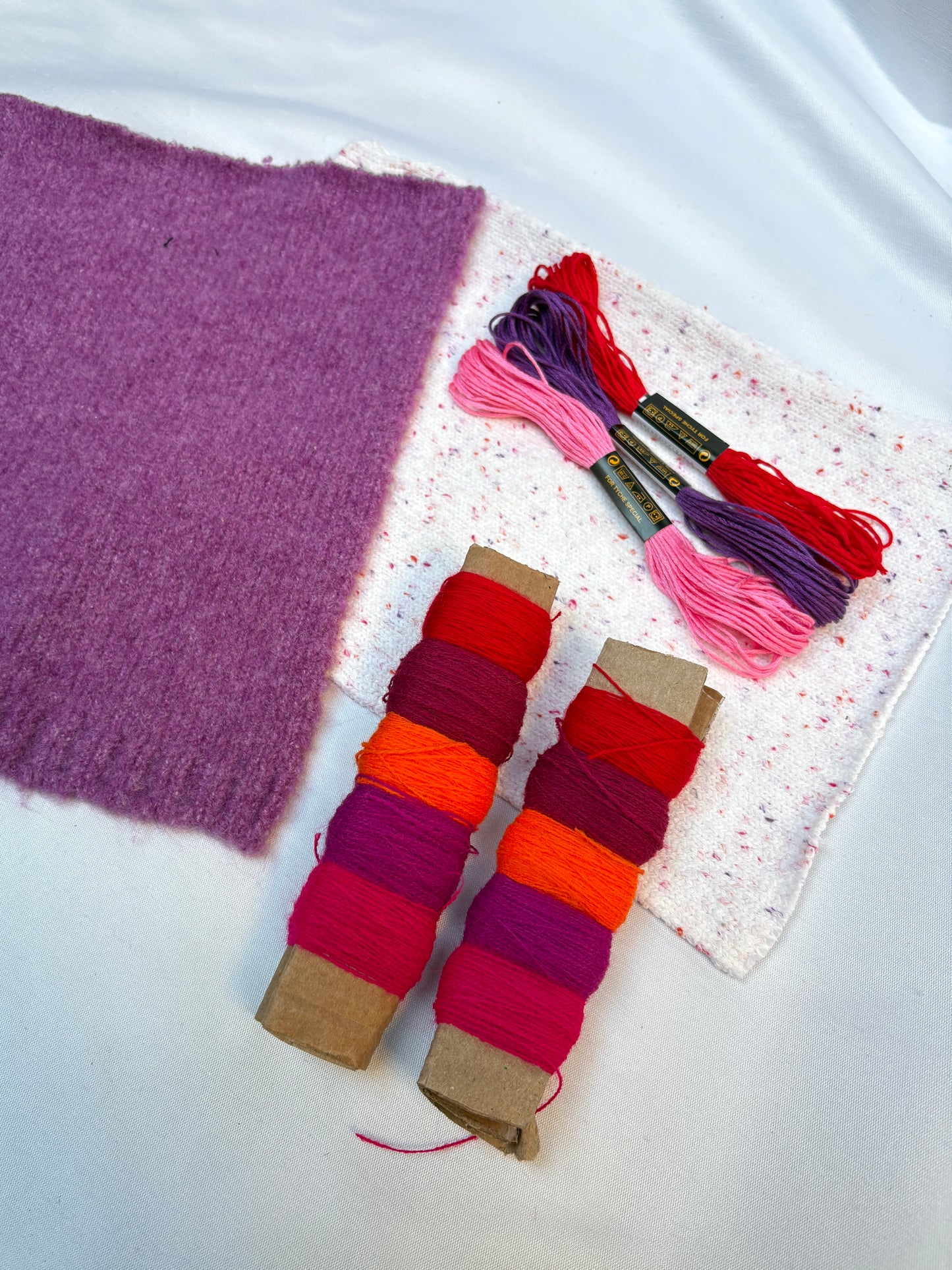 Soft fabric swatches with bright thread spools and embroidery floss.