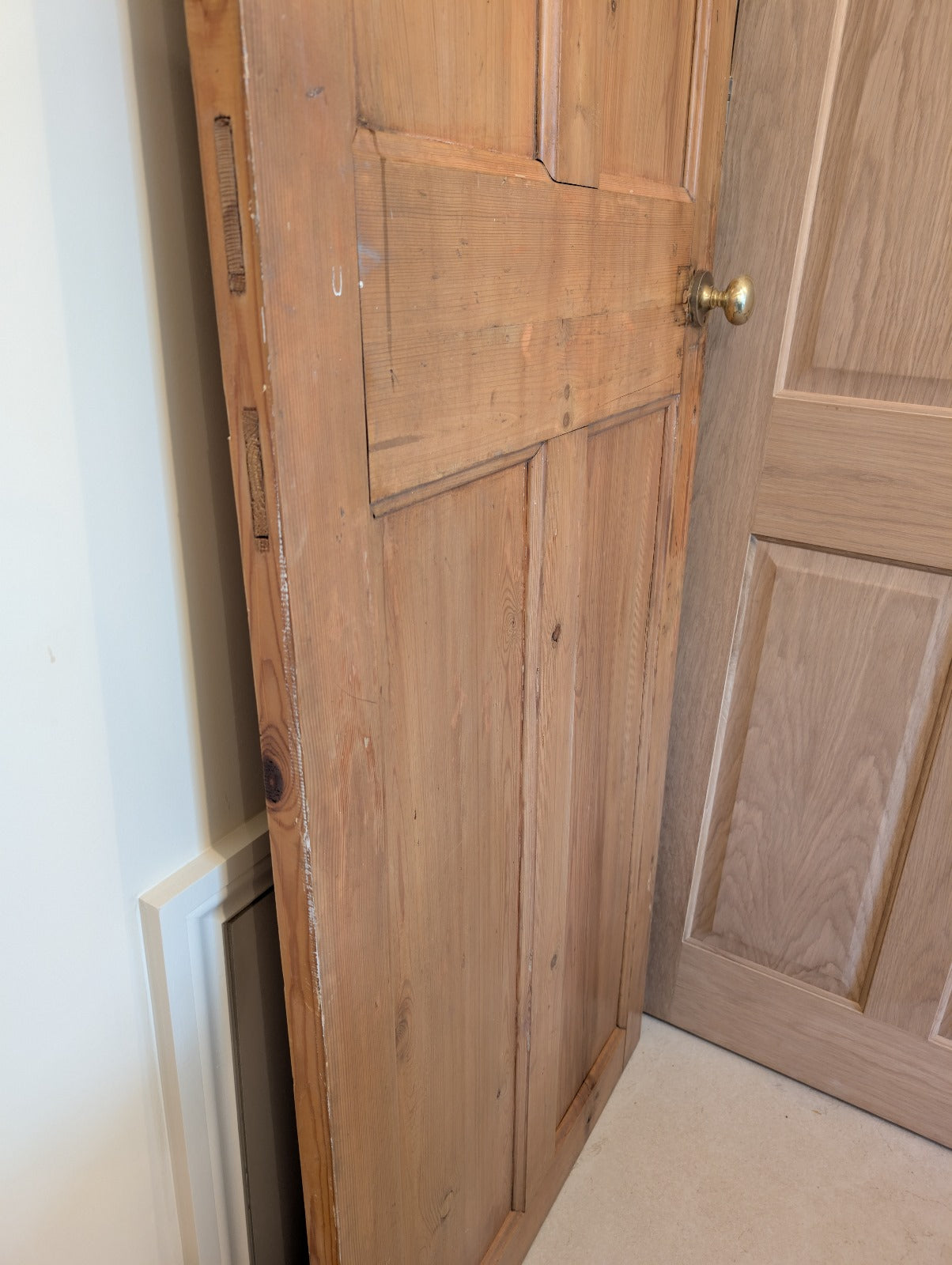 Vintage wooden interior door panel with brass knob leaning against a wall.