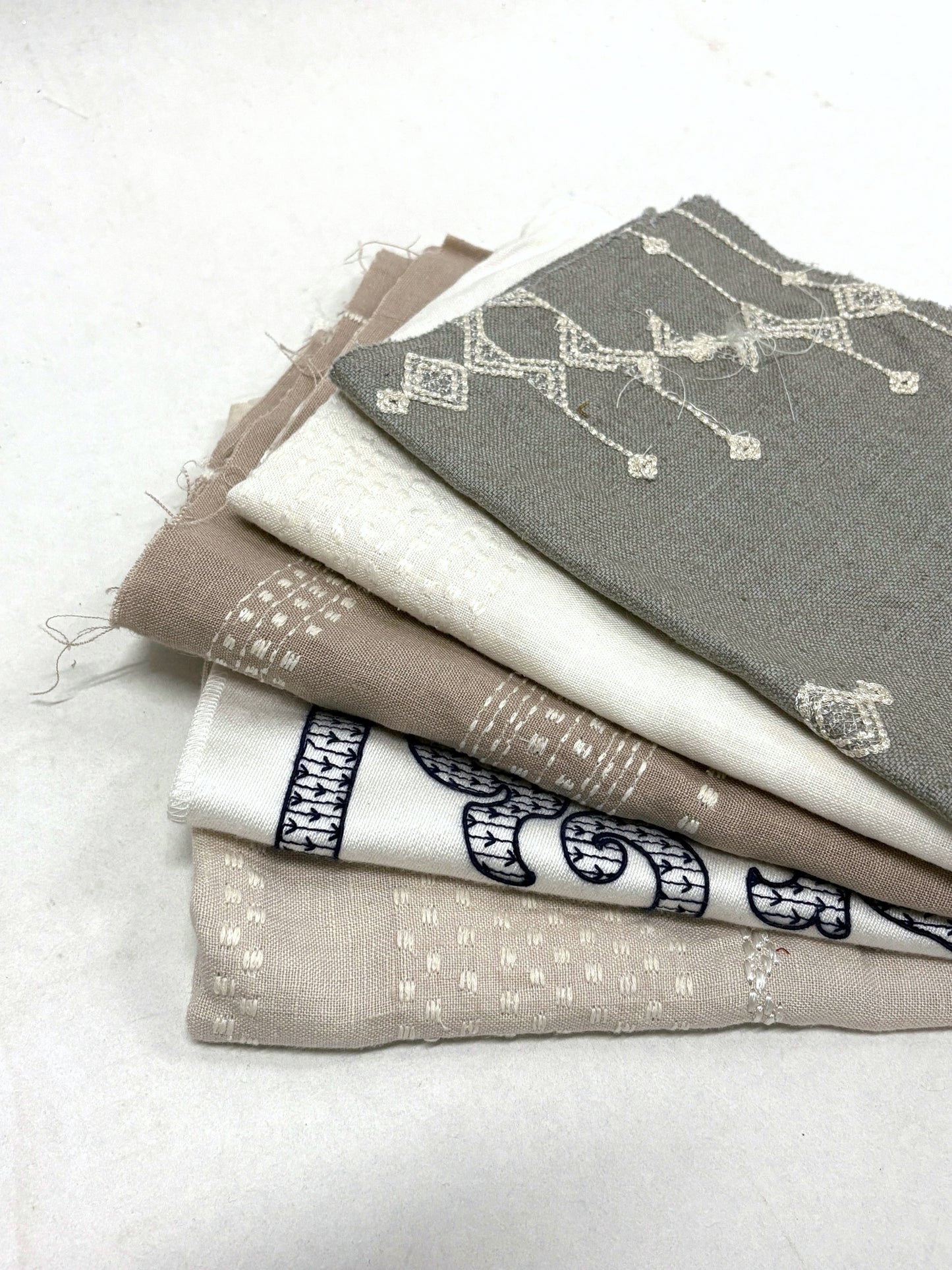 Stack of embroidered fabric samples with various patterns and colours.