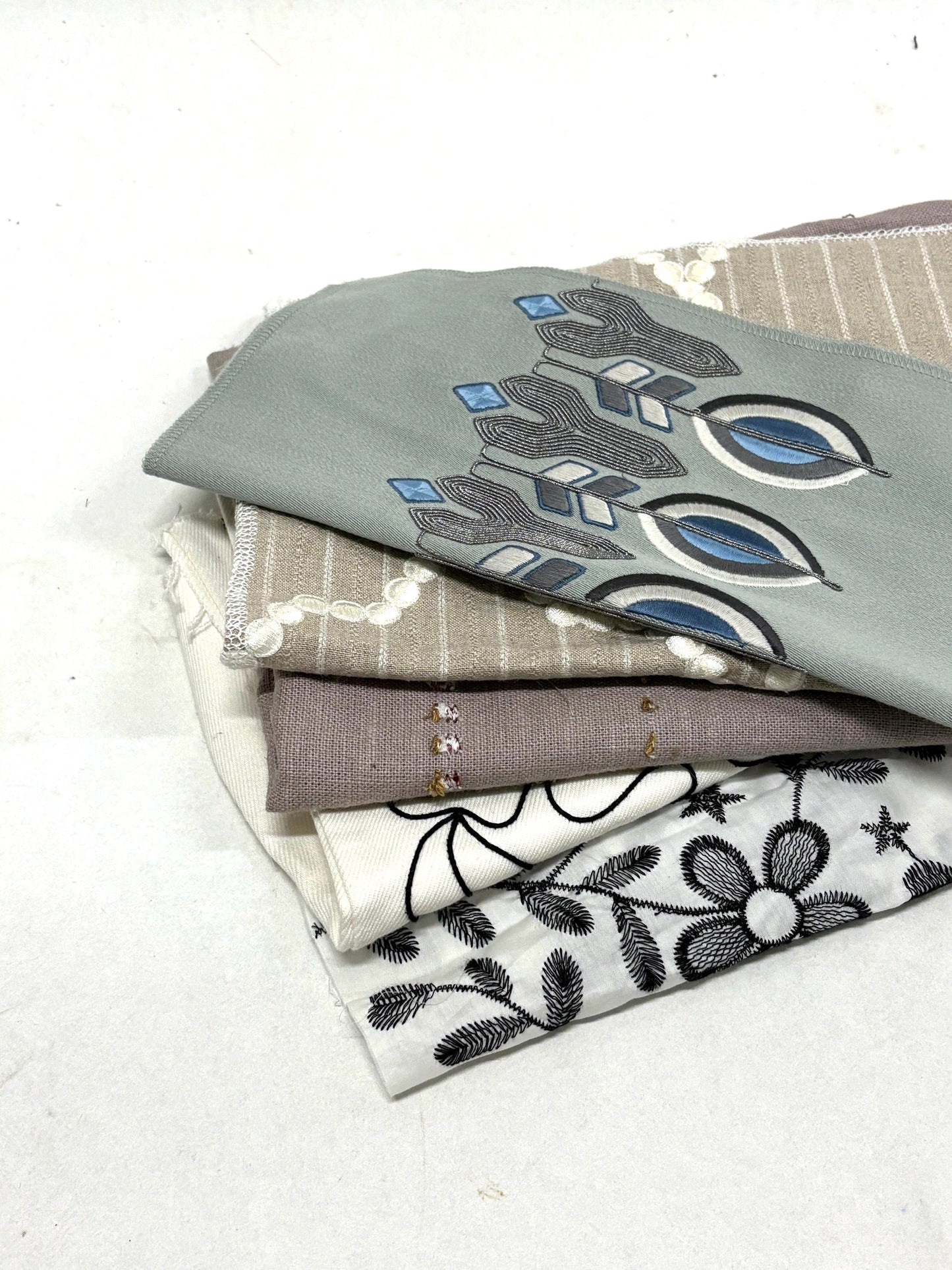 Stack of embroidered fabric samples with various patterns and colours.