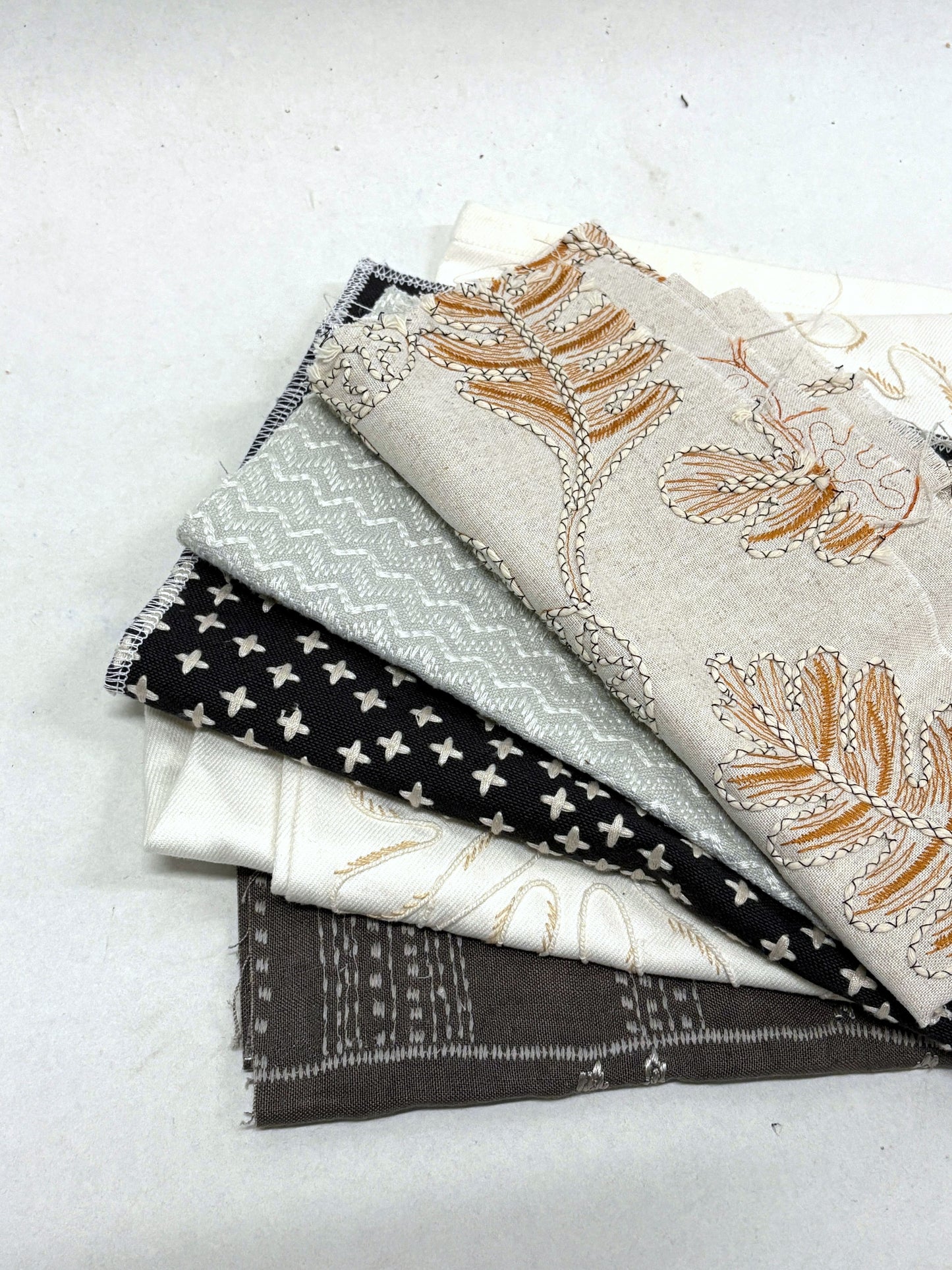 Stack of embroidered fabric samples with various patterns and colours.