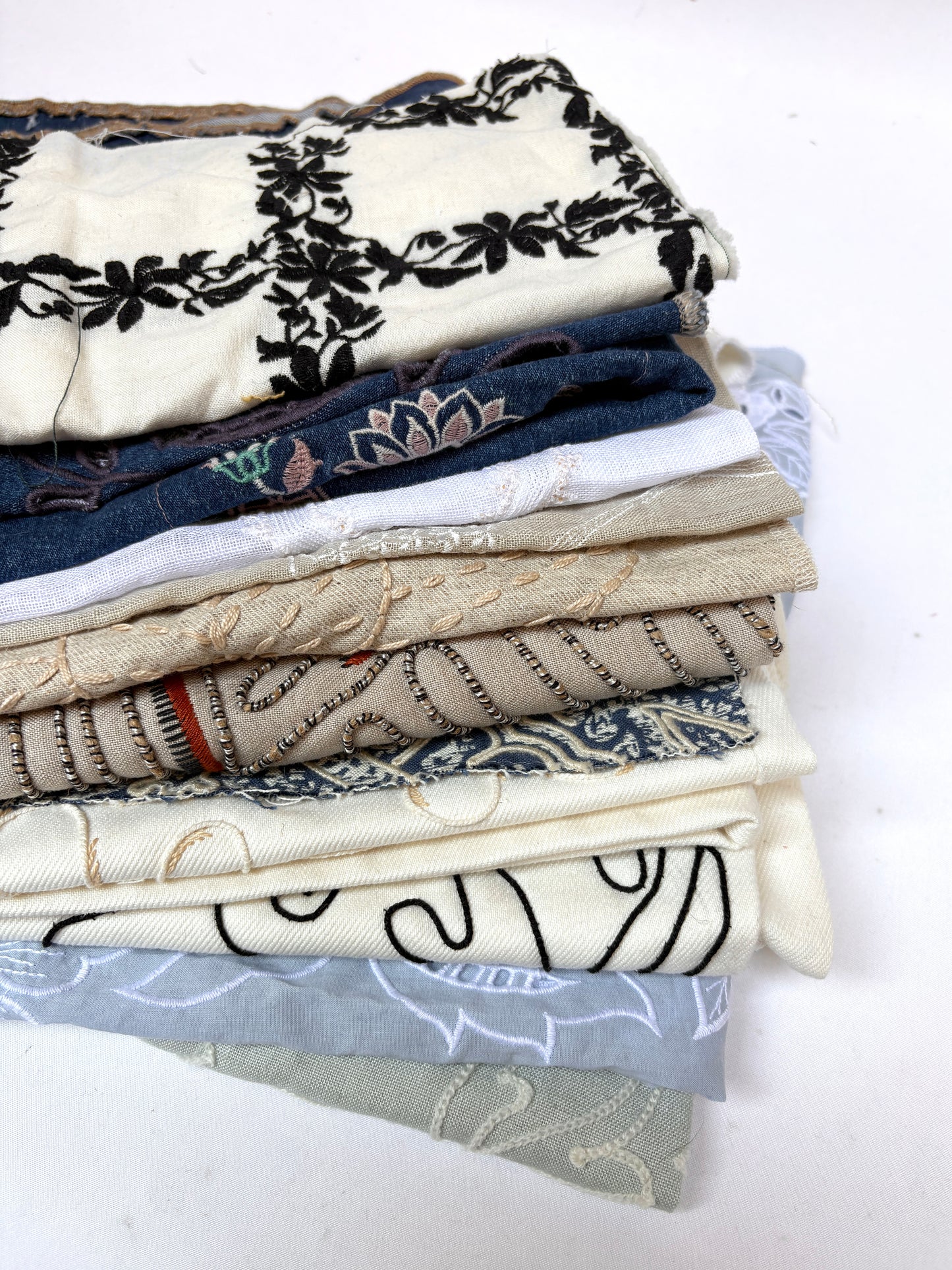 Stack of embroidered fabric samples with various patterns and colours.