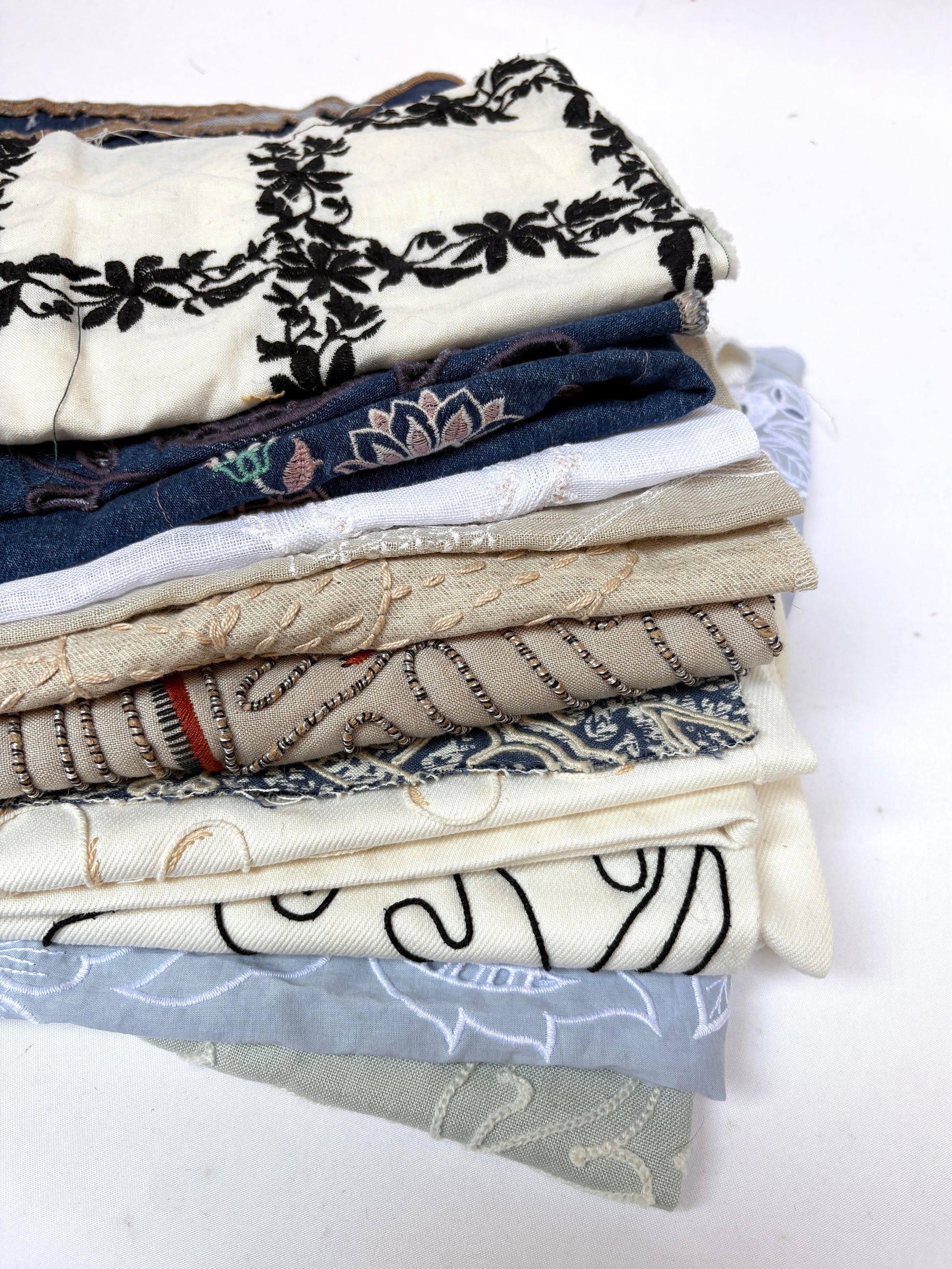 Stack of embroidered fabric samples with various patterns and colours.