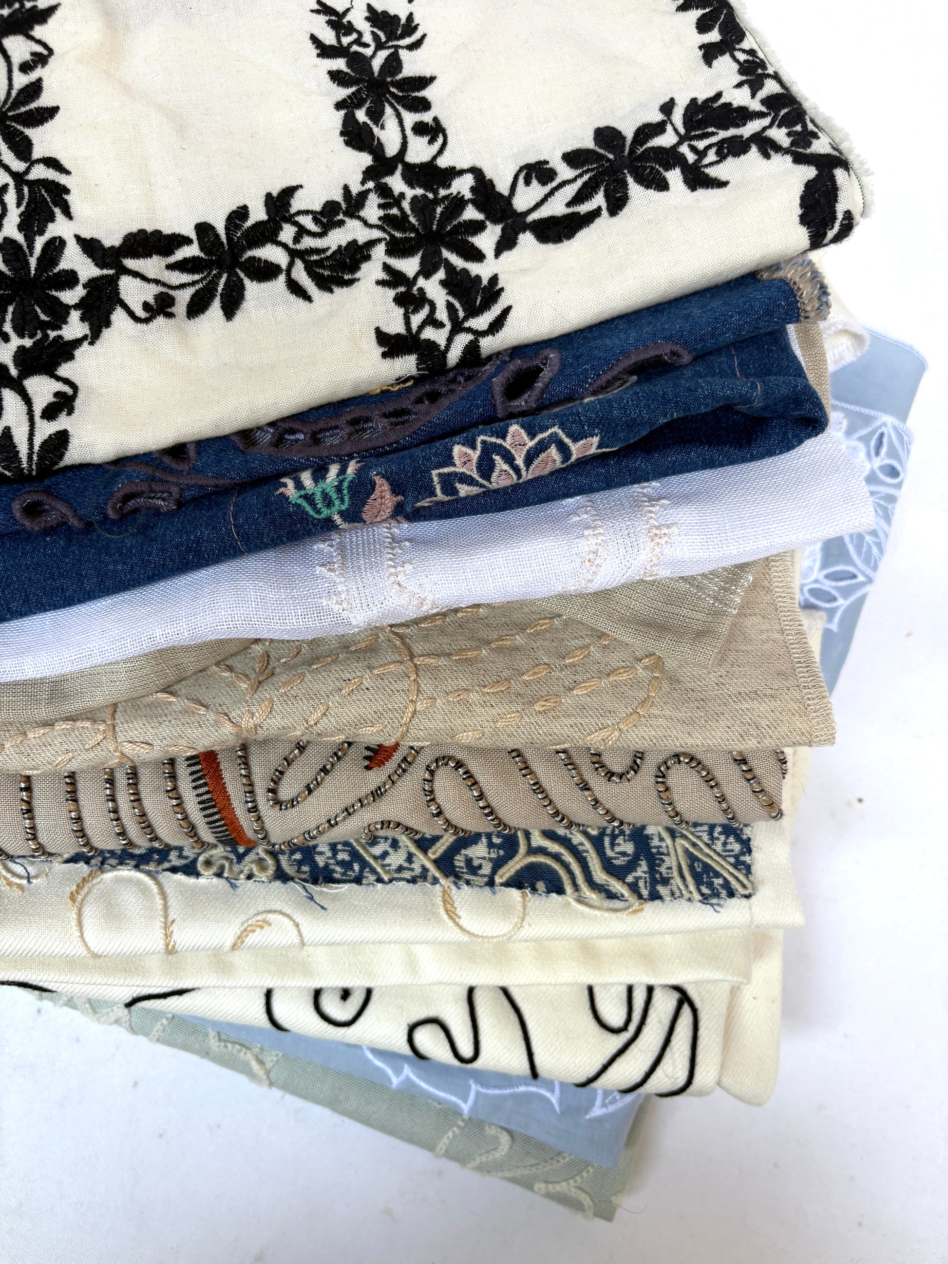 Stack of embroidered fabric samples with various patterns and colours.