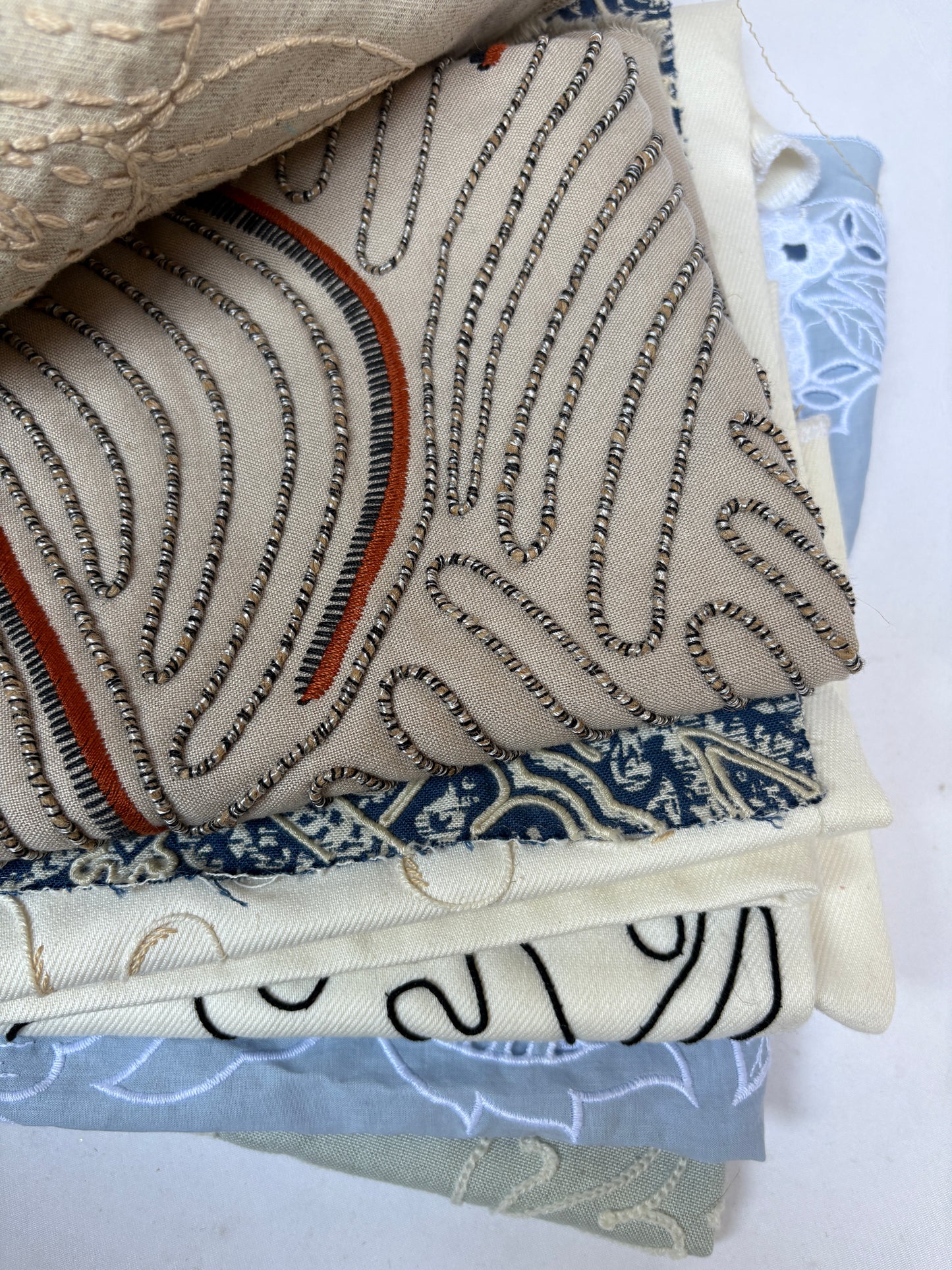 Stack of embroidered fabric samples with various patterns and colours.