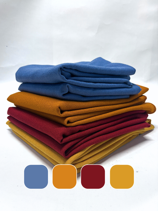 Stack of folded wool crepe fabric in blue, brown, yellow, and red with colour swatches below
