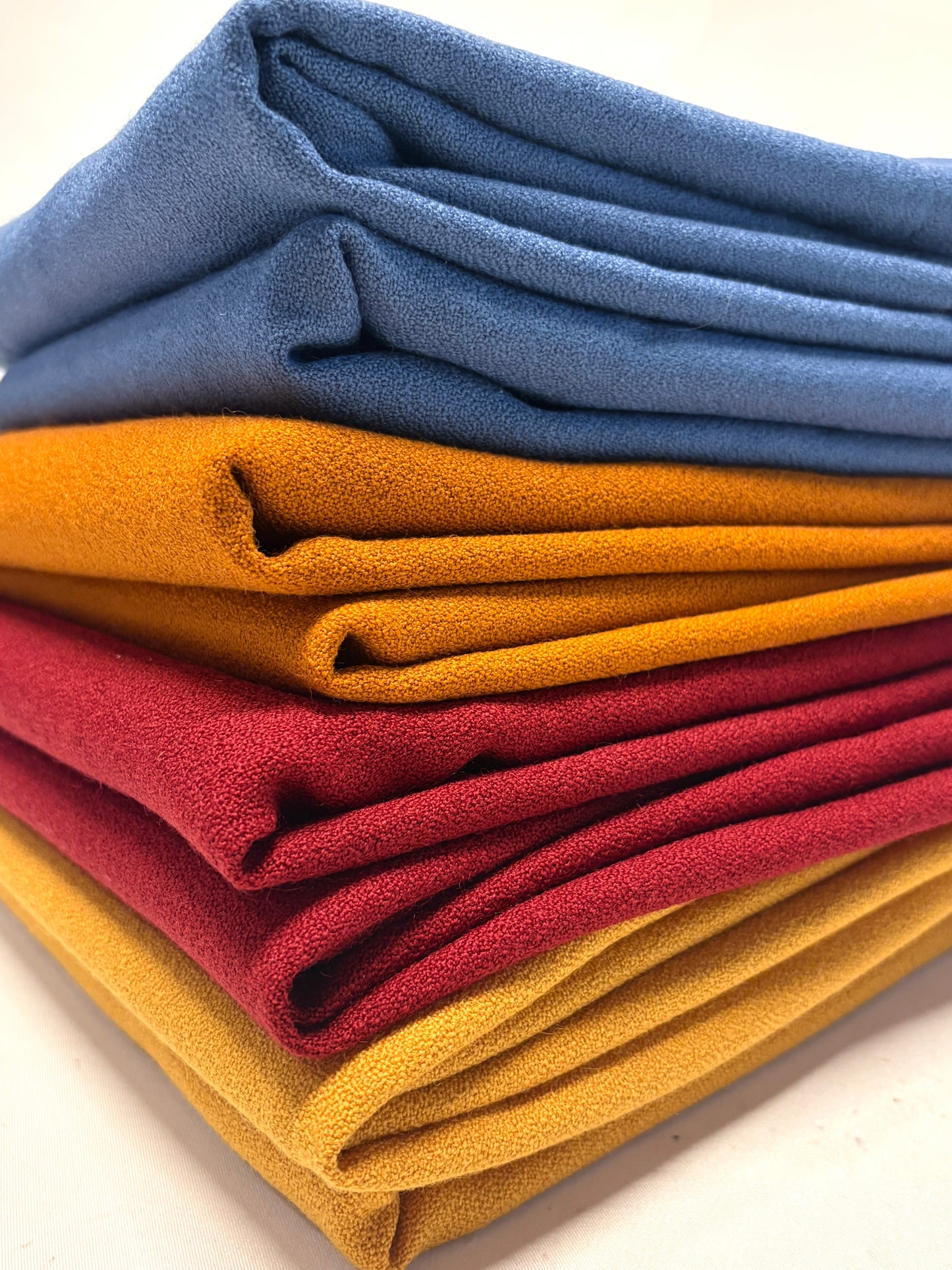 Stack of folded wool crepe fabric in blue, brown, yellow, and red 