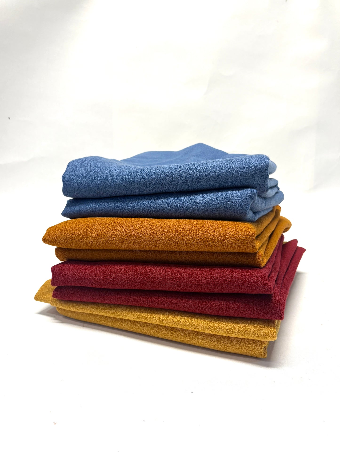 Stack of folded wool crepe fabric in blue, brown, yellow, and red 