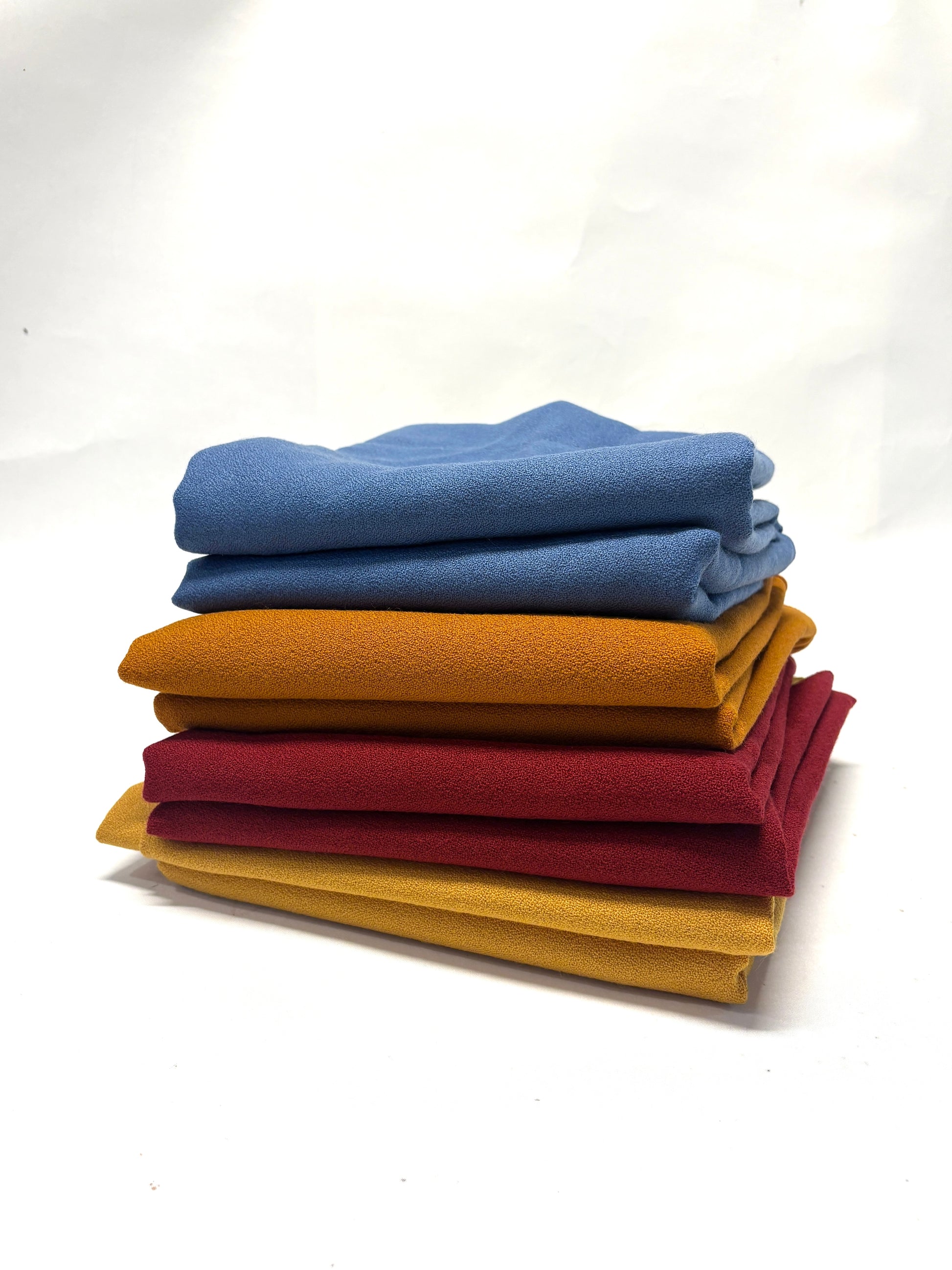 Stack of folded wool crepe fabric in blue, brown, yellow, and red 