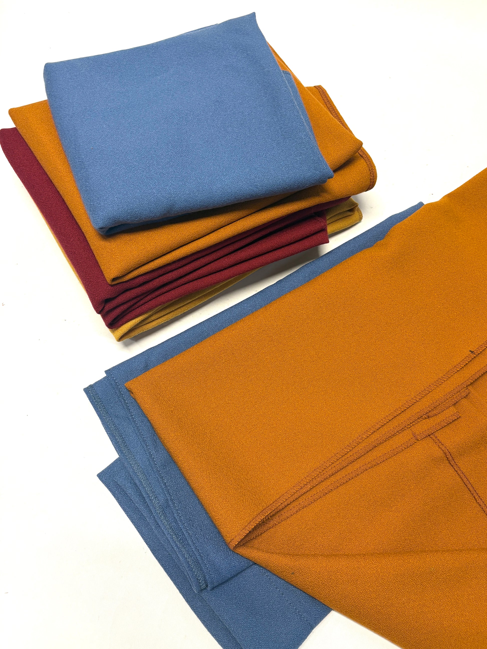 Stack of folded wool crepe fabric in blue, brown, yellow, and red 