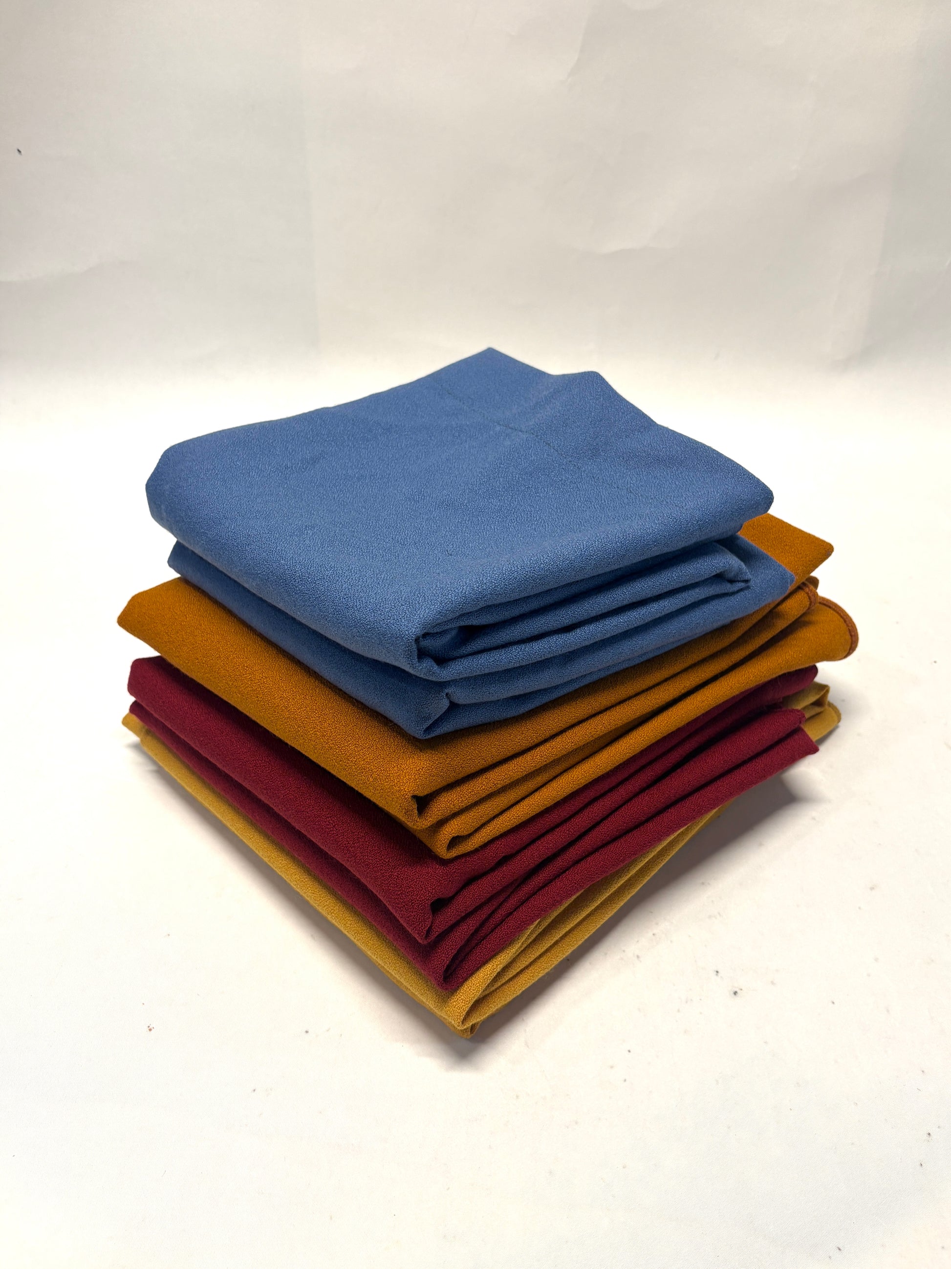 Stack of folded wool crepe fabric in blue, brown, yellow, and red 