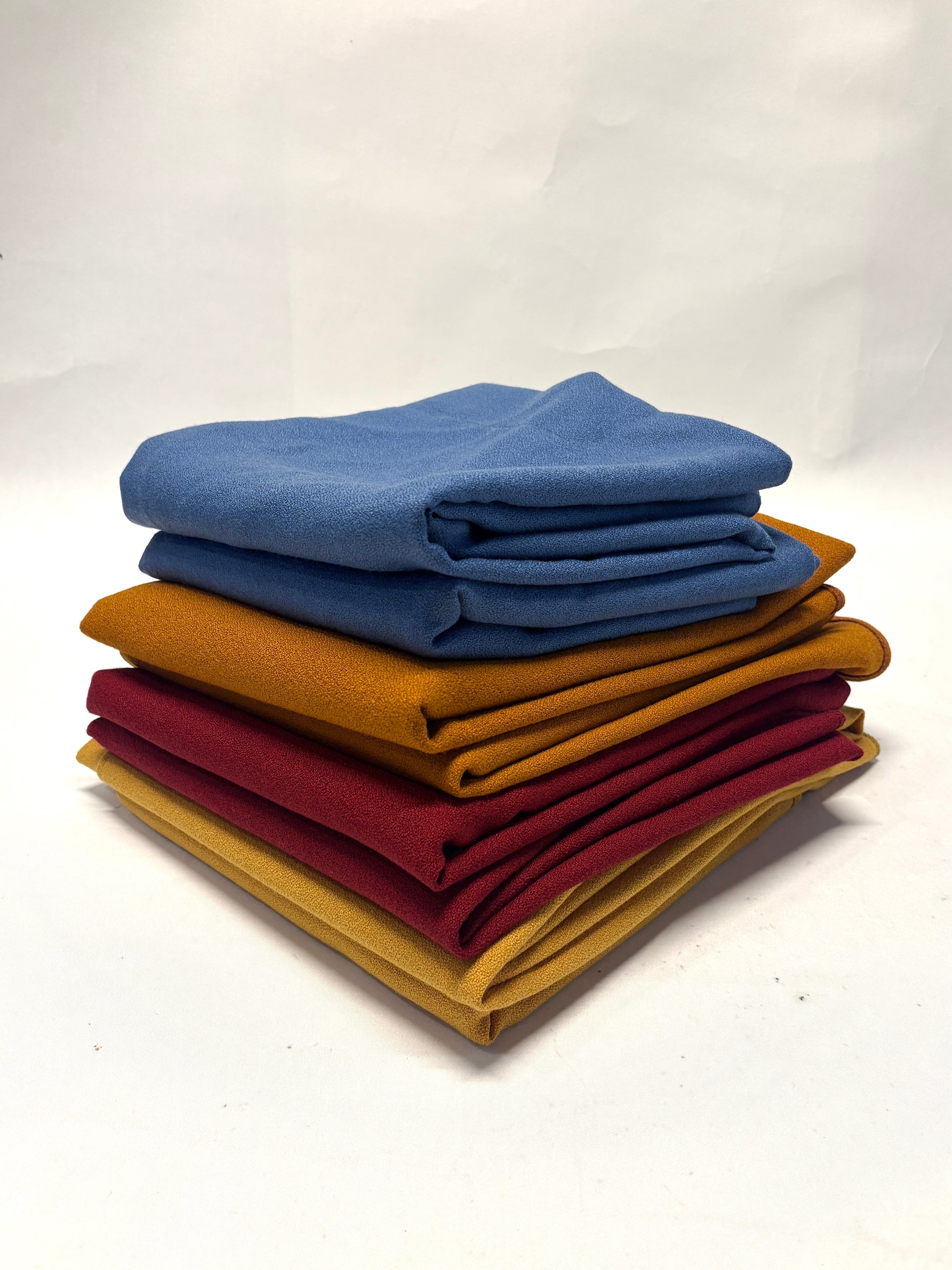 Stack of folded wool crepe fabric in blue, brown, yellow, and red 