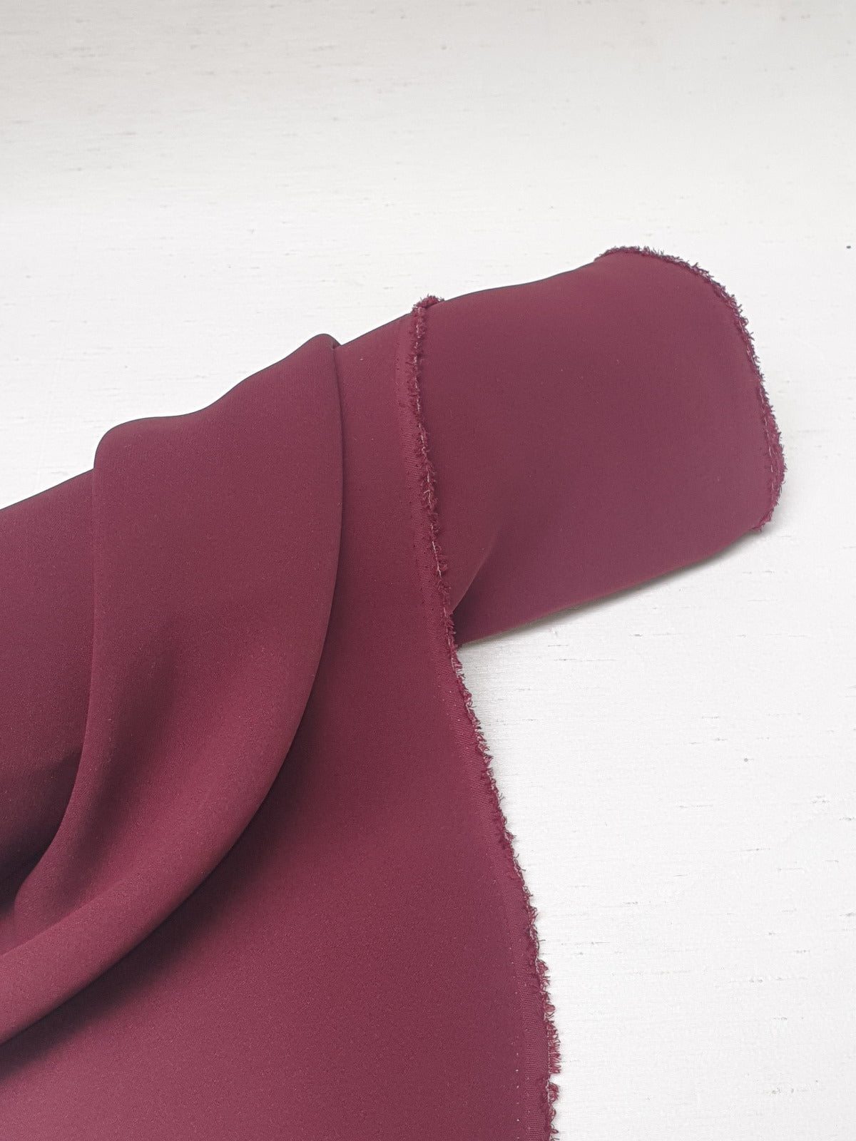 Close-up of light weighted fabric in burgundy, soft texture visible 