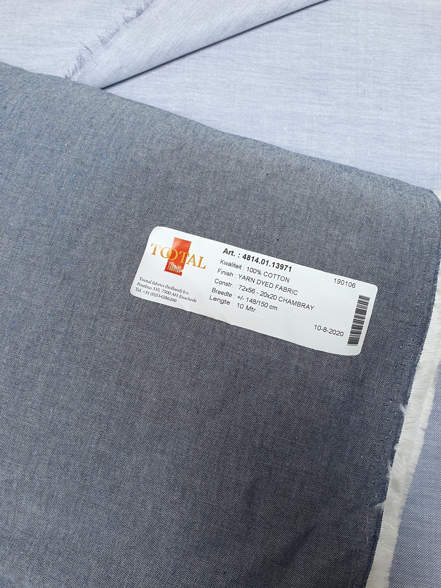 Close-up of chambray cotton fabric in blue-grey with a sticker that contains its details 