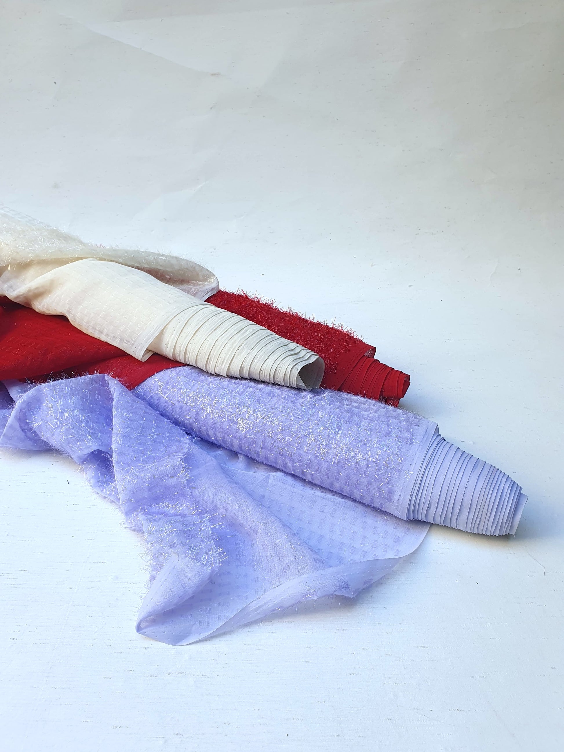 Three rolls of sparkly embroidered fabric in red, lilac and cream