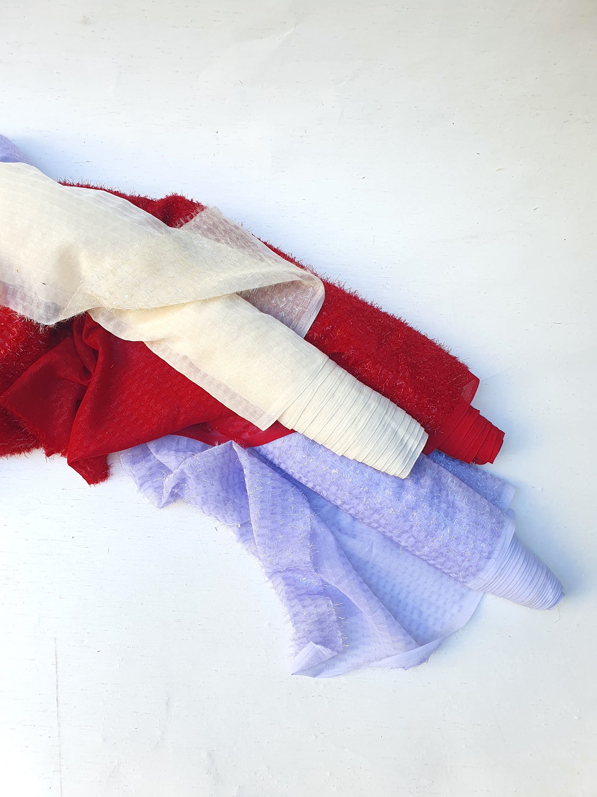 Three rolls of sparkly embroidered fabric in red, lilac and cream