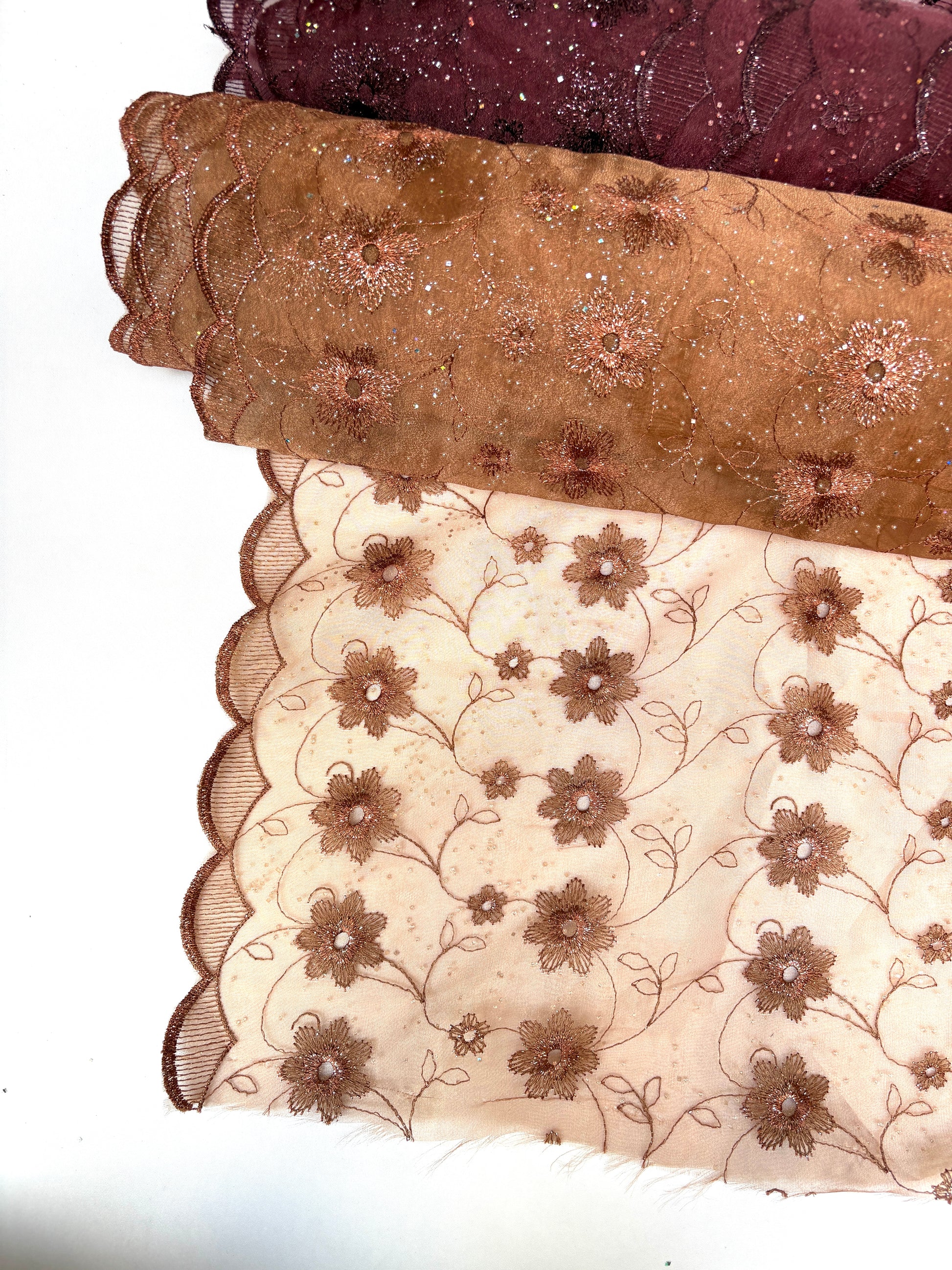 Close-up of embroidered lace fabric with floral patterns in brown and red tones.