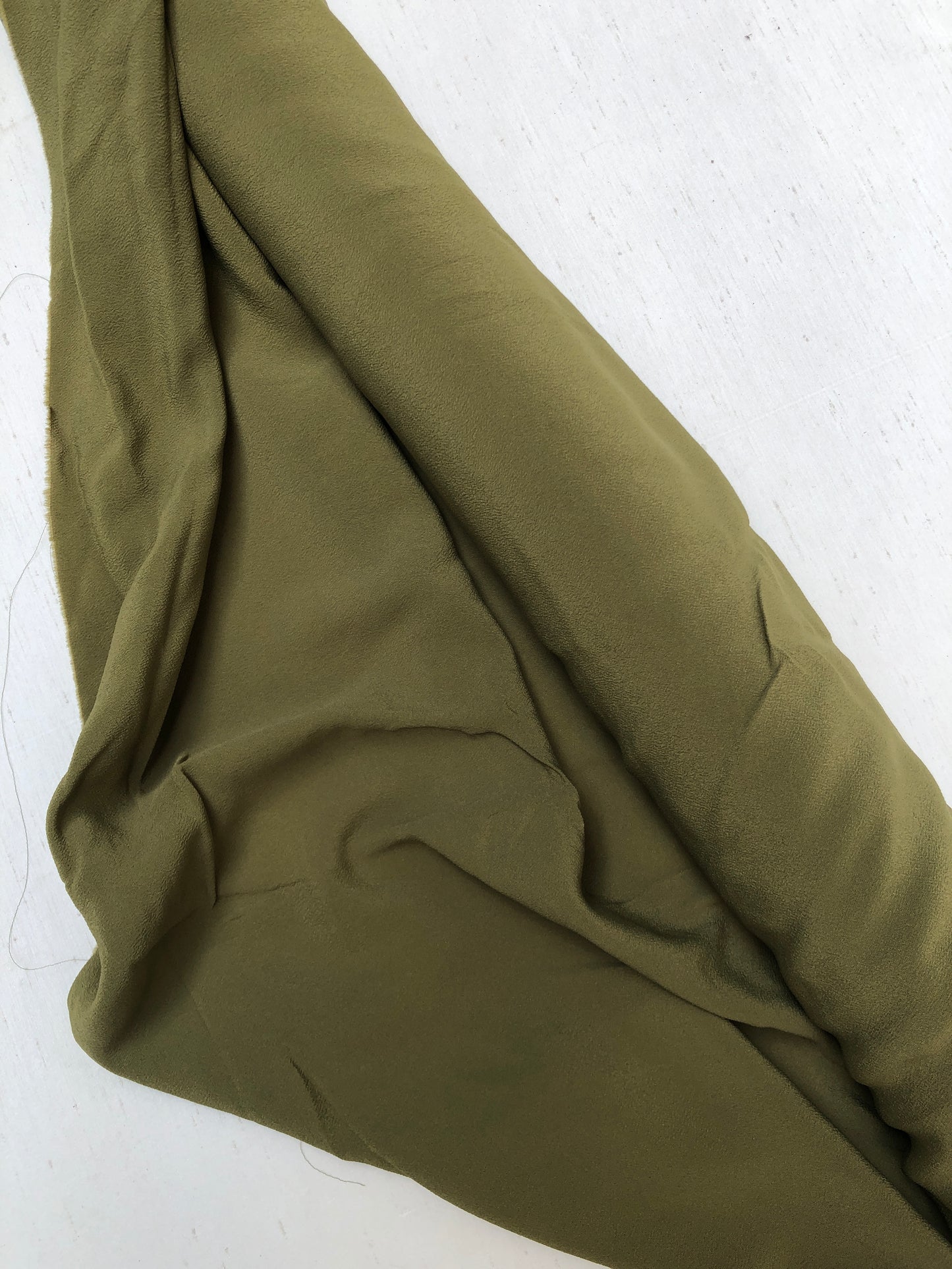 Roll of light weighted crape fabric in olive green, soft texture visible 