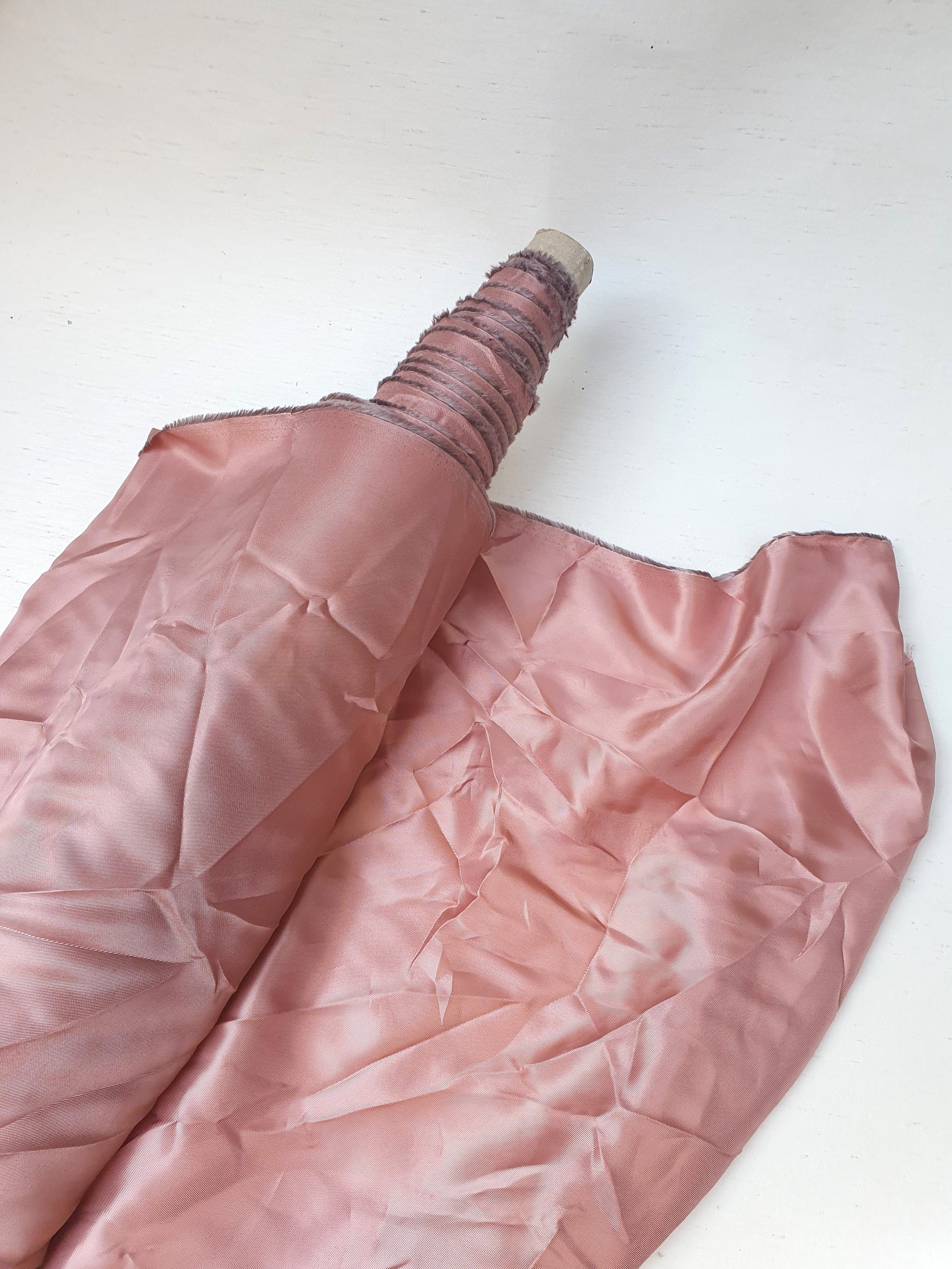 Roll of satin twill fabric in pink, shiny texture visible 