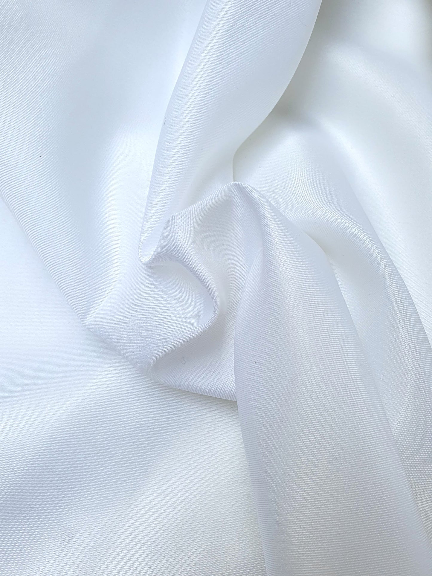 Close-up of shiny polyester taffeta fabric in white, soft texture visible 