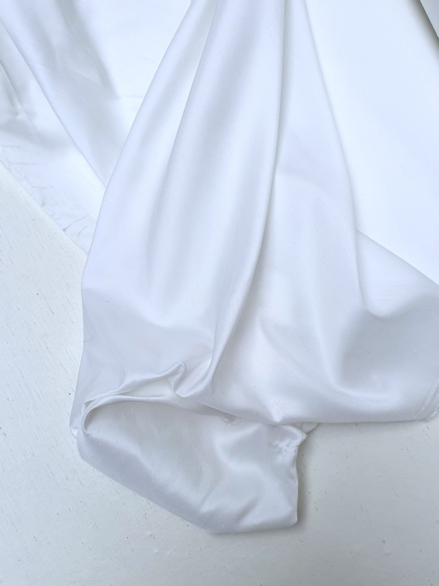 Close-up of shiny polyester taffeta fabric in white, soft texture visible 
