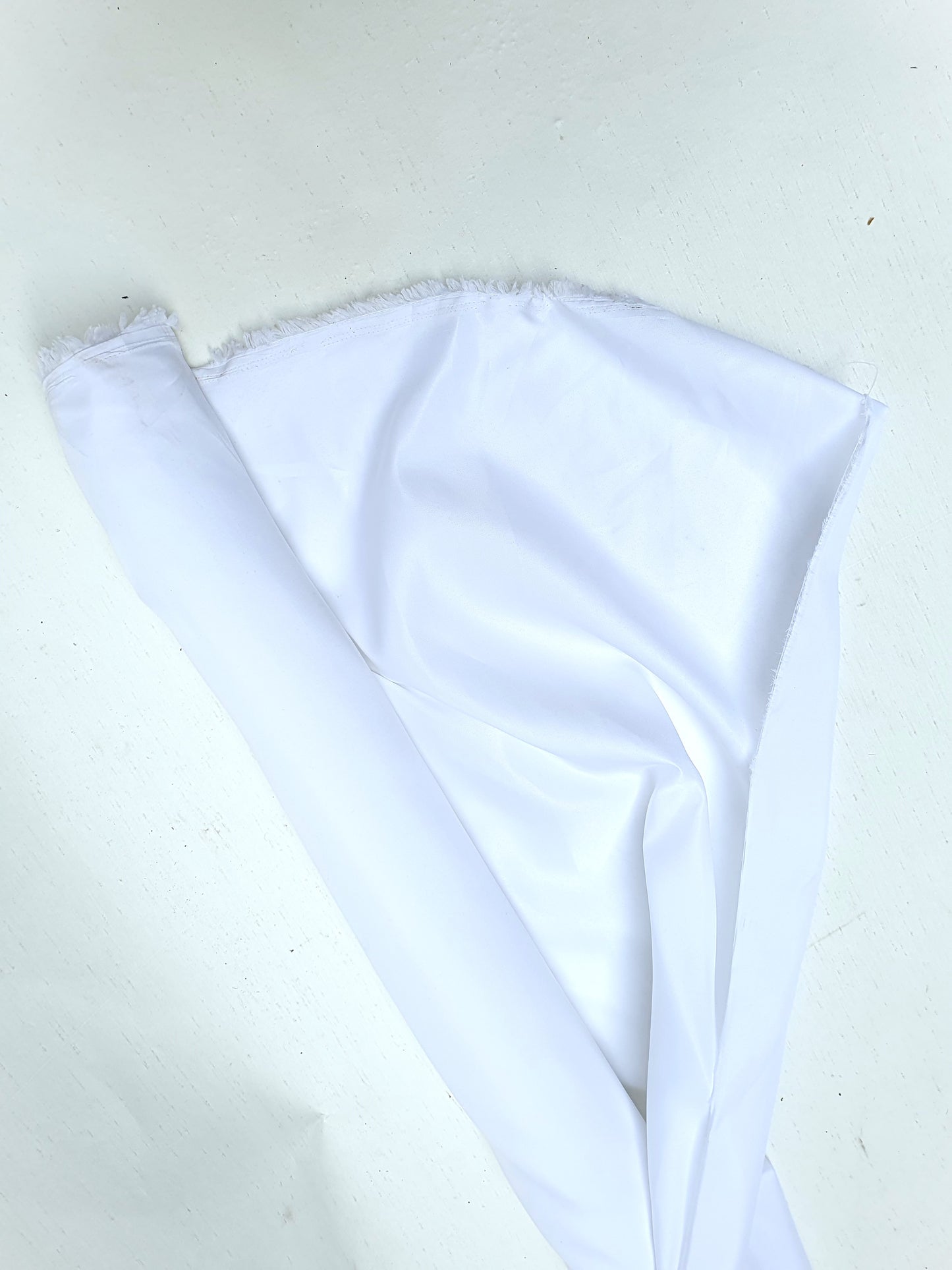 Roll of shiny polyester taffeta fabric in white, soft texture visible 