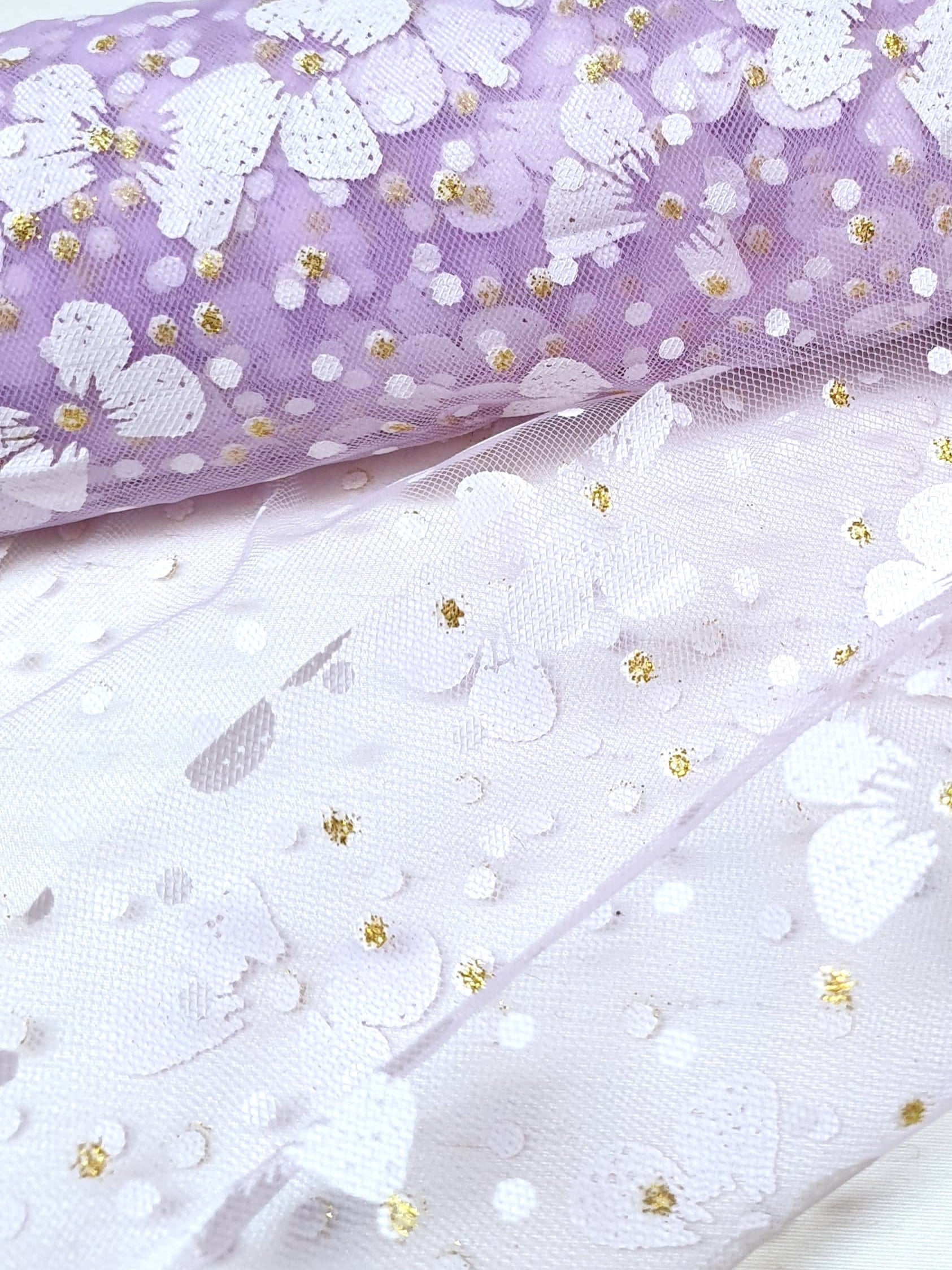 Close-up of a roll of floral printed transparent mesh fabric in purple
