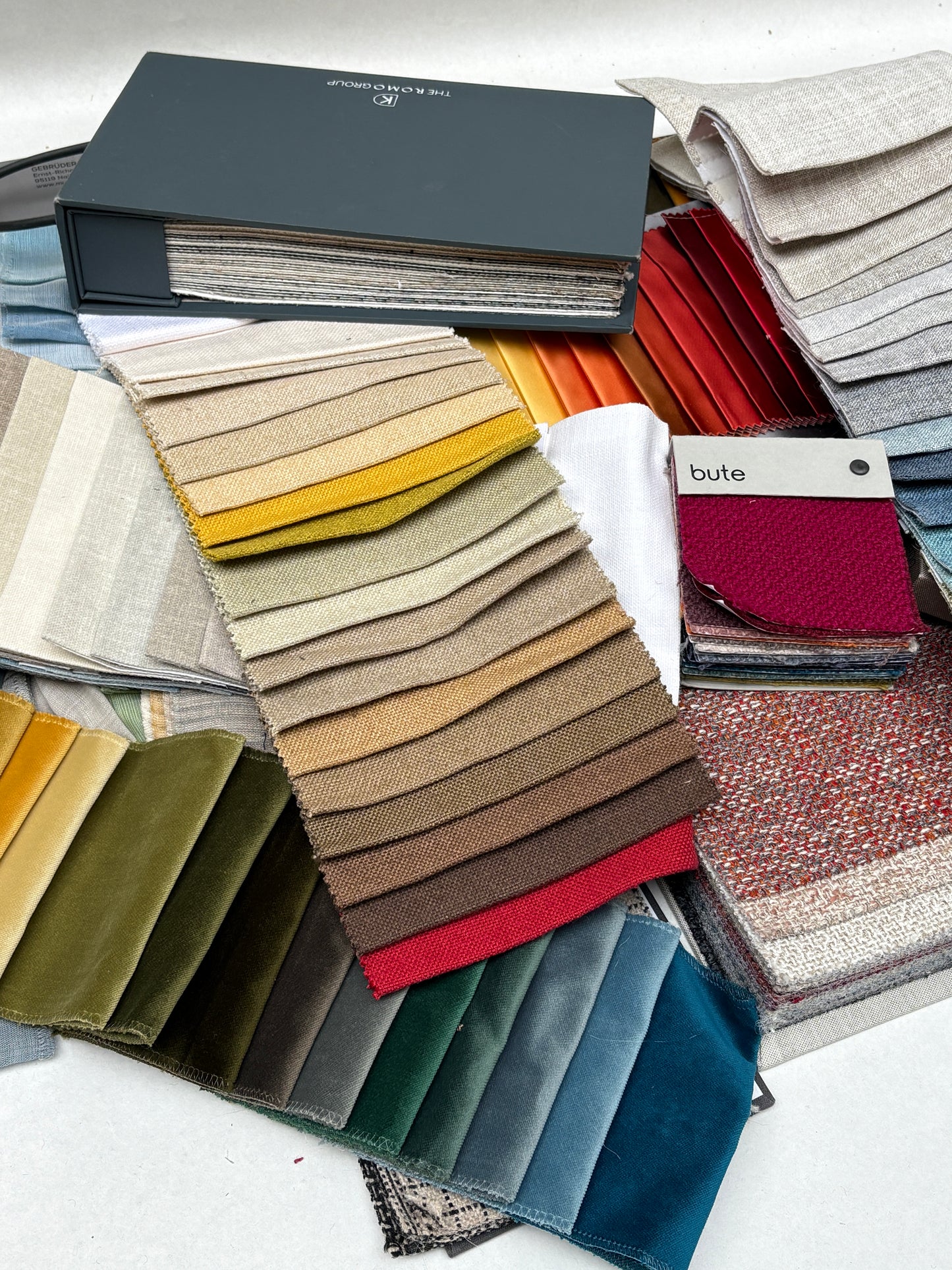 Layered fabric swatches in many colours are spread across a white surface