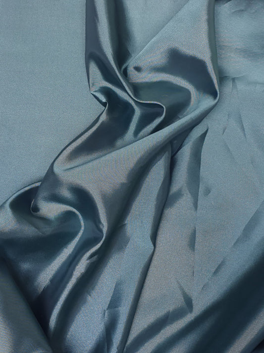 Close-up of iridescent turquoise satin fabric with a smooth texture, showing light reflections on its surface.