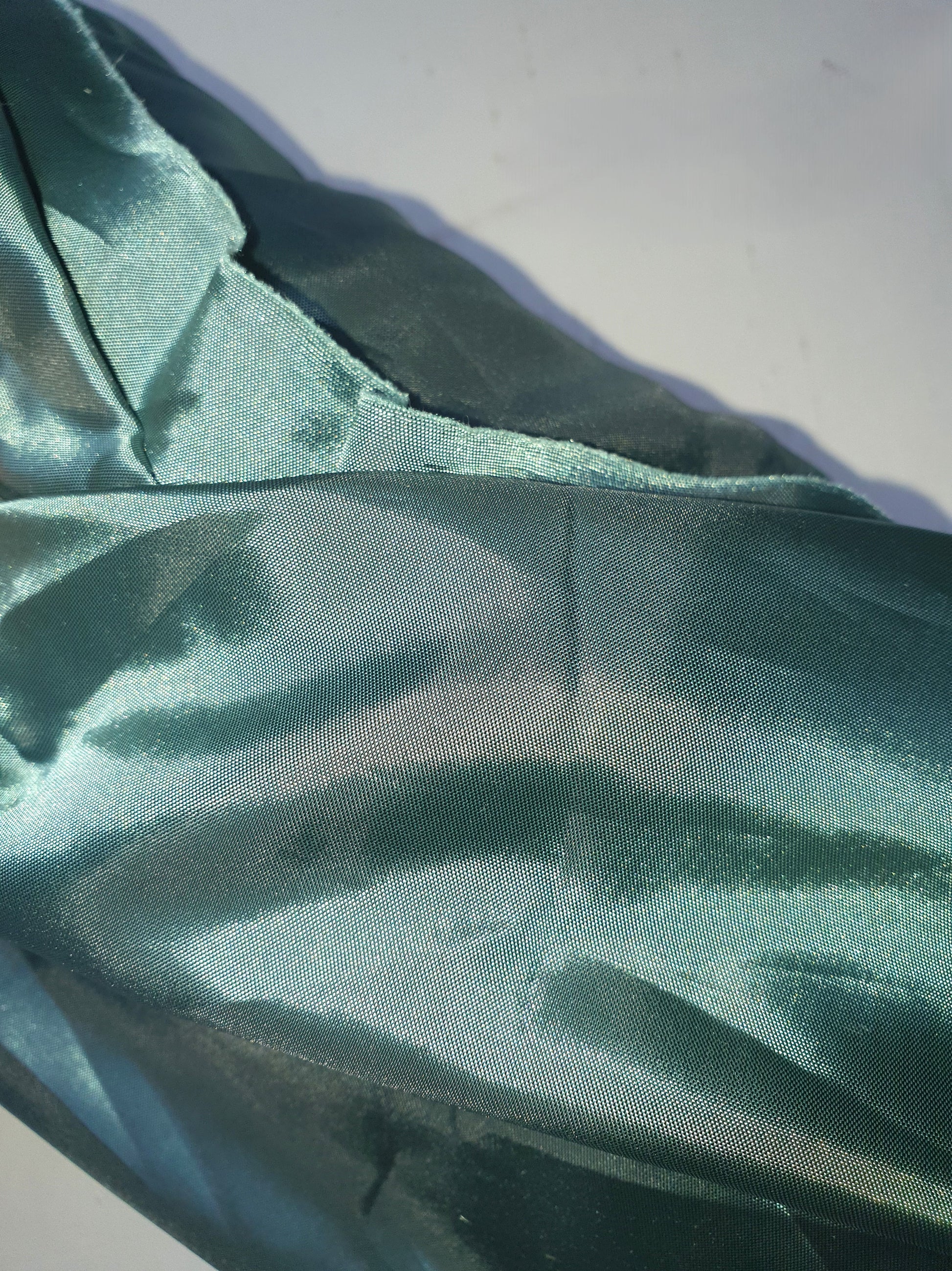 Close-up of a roll of iridescent turquoise satin fabric with a smooth texture, showing light reflections on its surface.