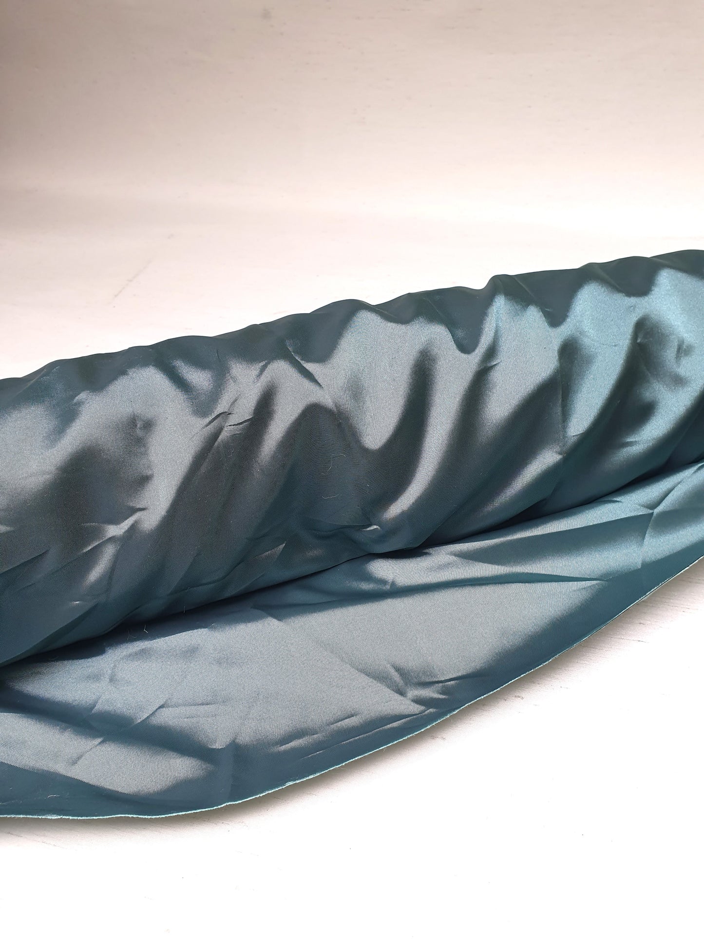 A roll of iridescent turquoise satin fabric with a smooth texture, showing light reflections on its surface.