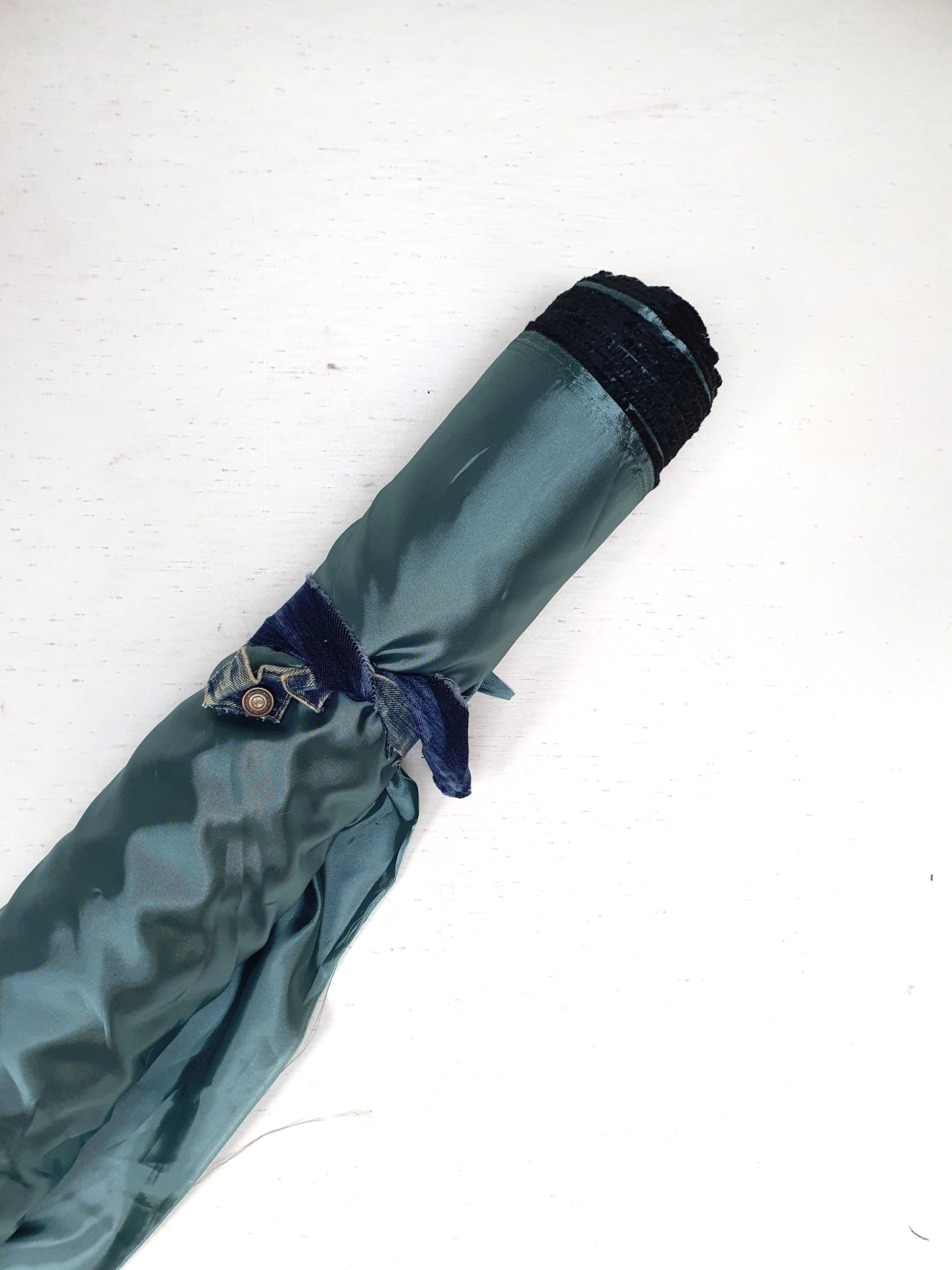 A roll of iridescent turquoise satin fabric with a smooth texture, showing light reflections on its surface.
