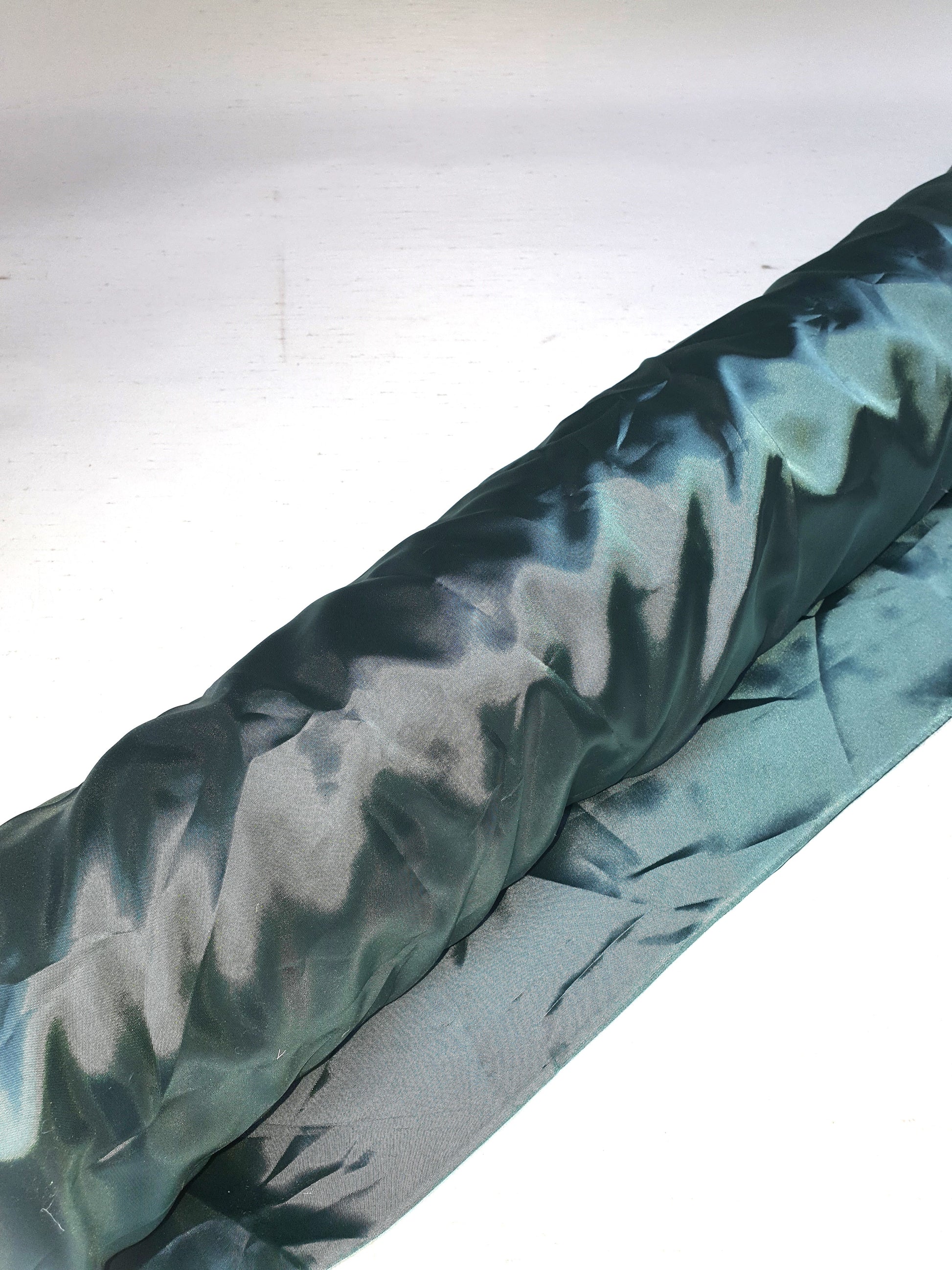 A roll of iridescent turquoise satin fabric with a smooth texture, showing light reflections on its surface.