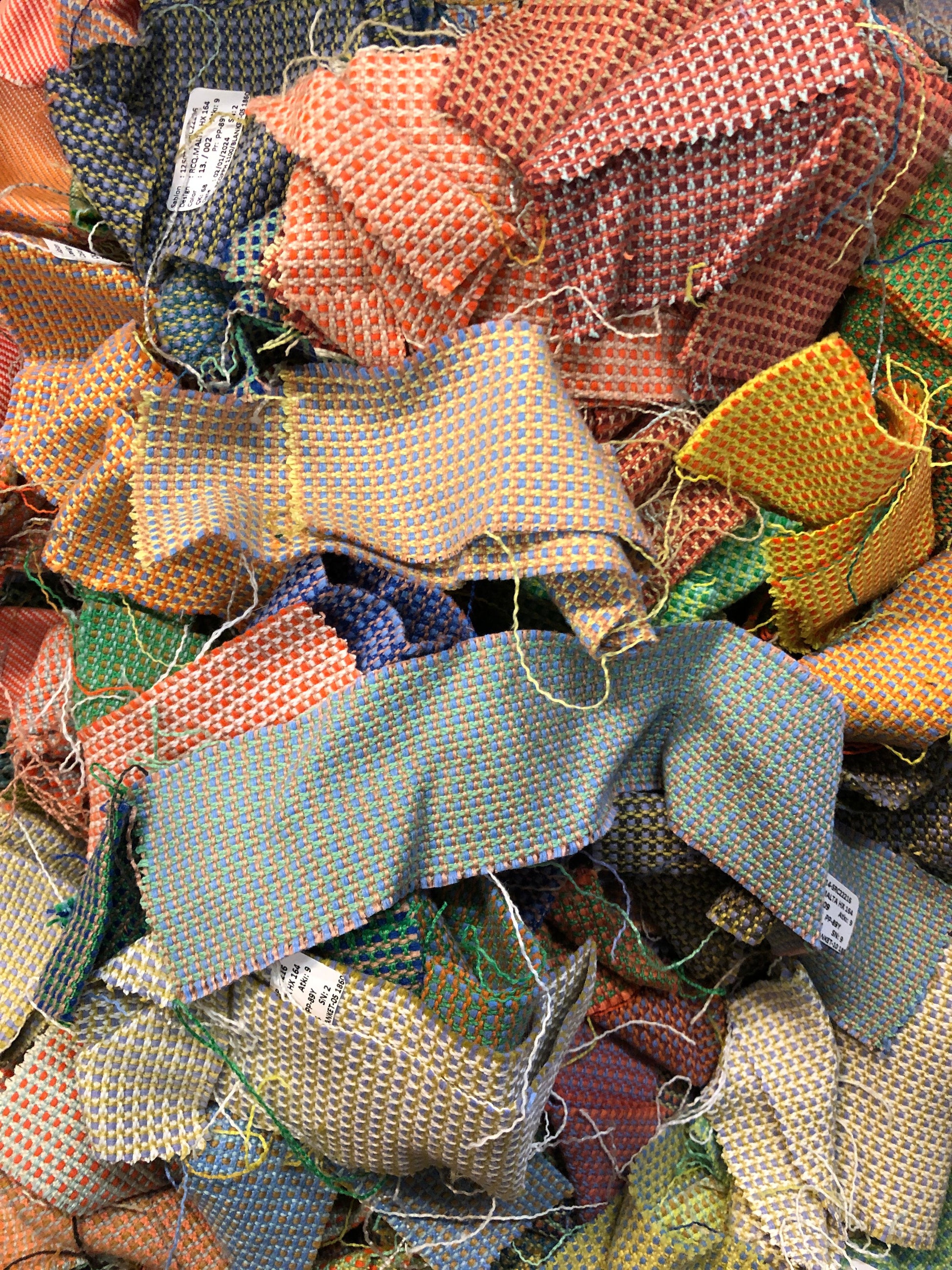 A pile of various rectangular fabric offcuts in different colours and textures.