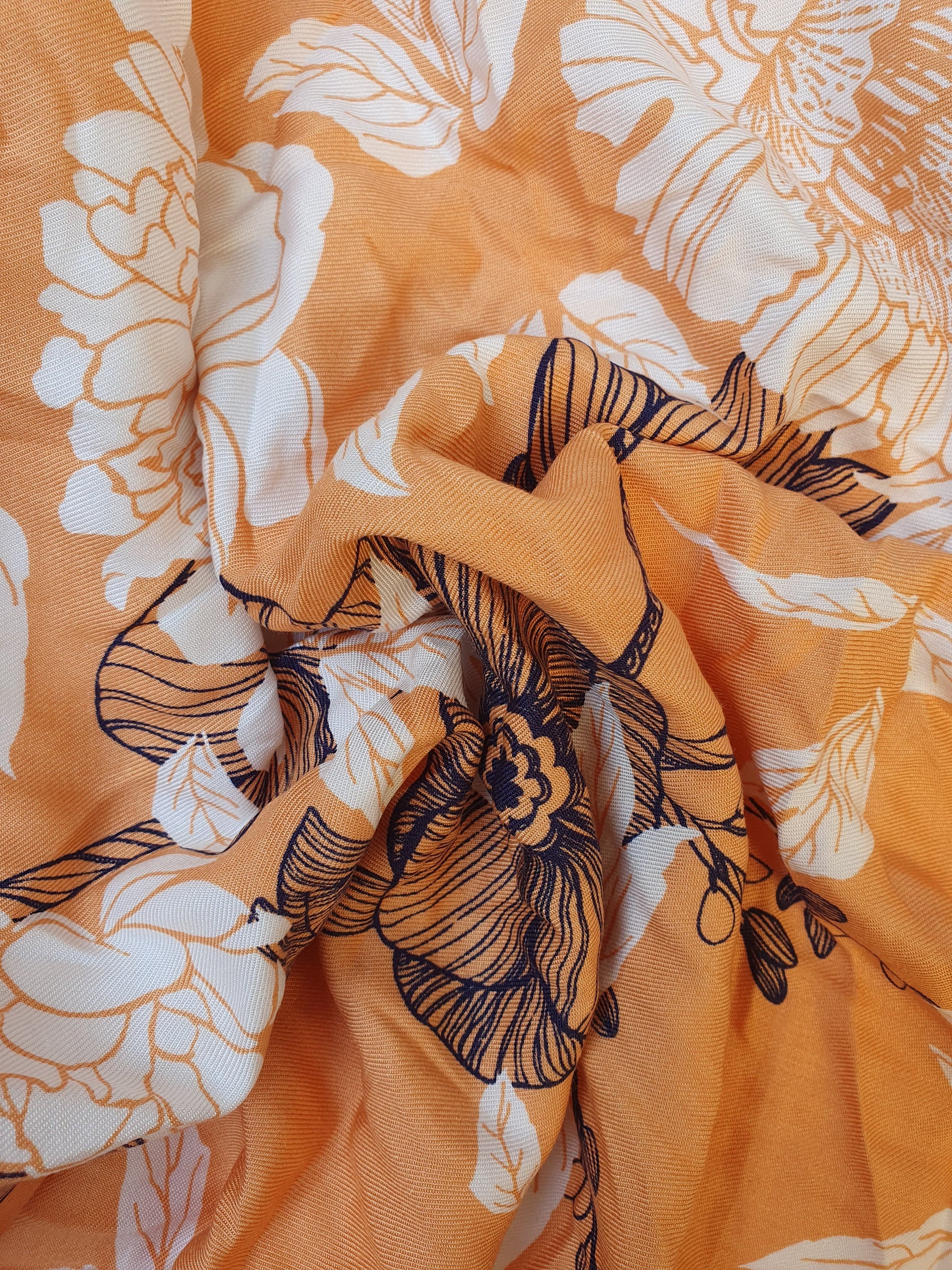 Close-up of orange floral fabric with white and navy botanical patterns.