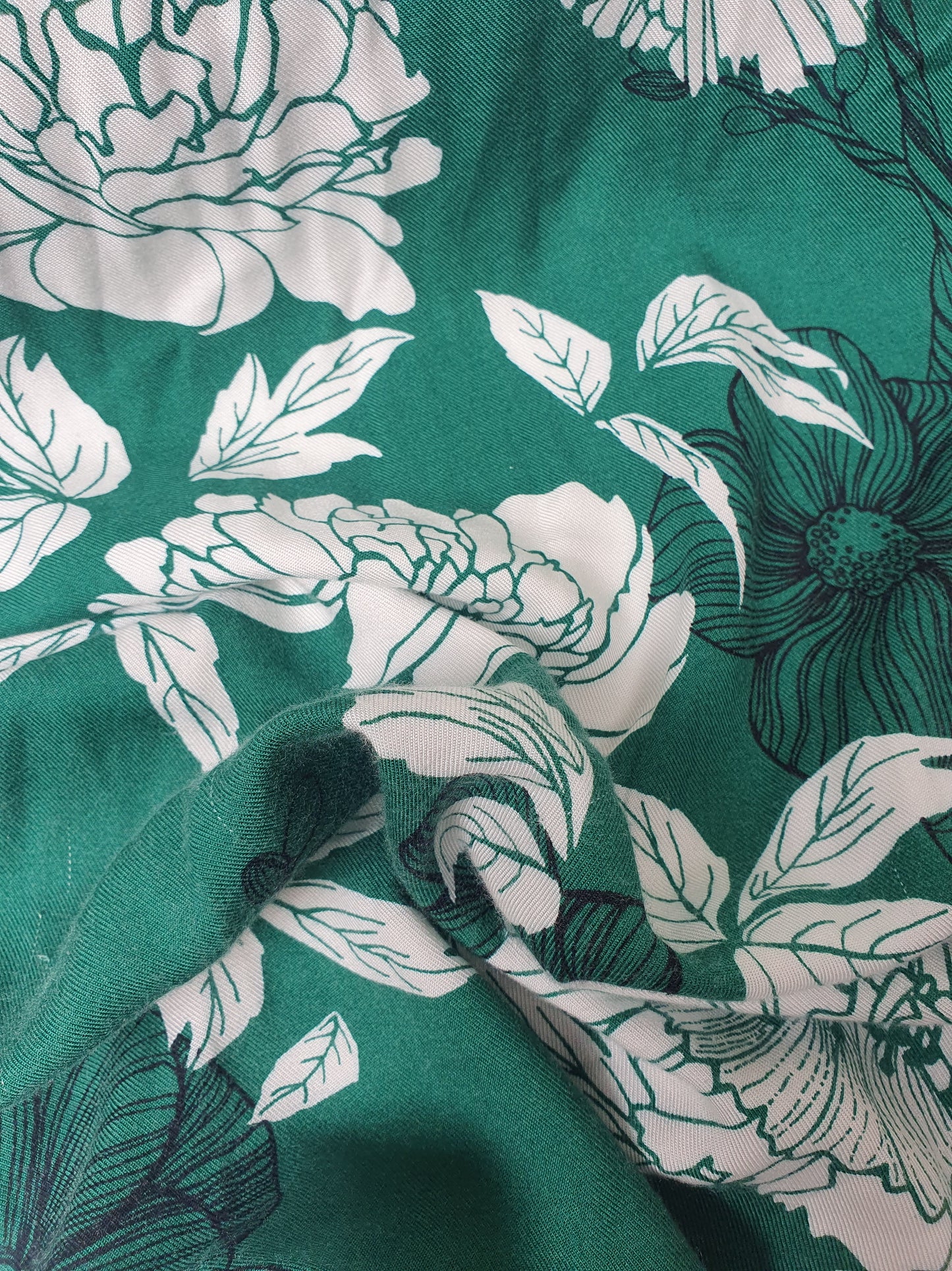 Close-up of green floral fabric with white and dark botanical patterns.
