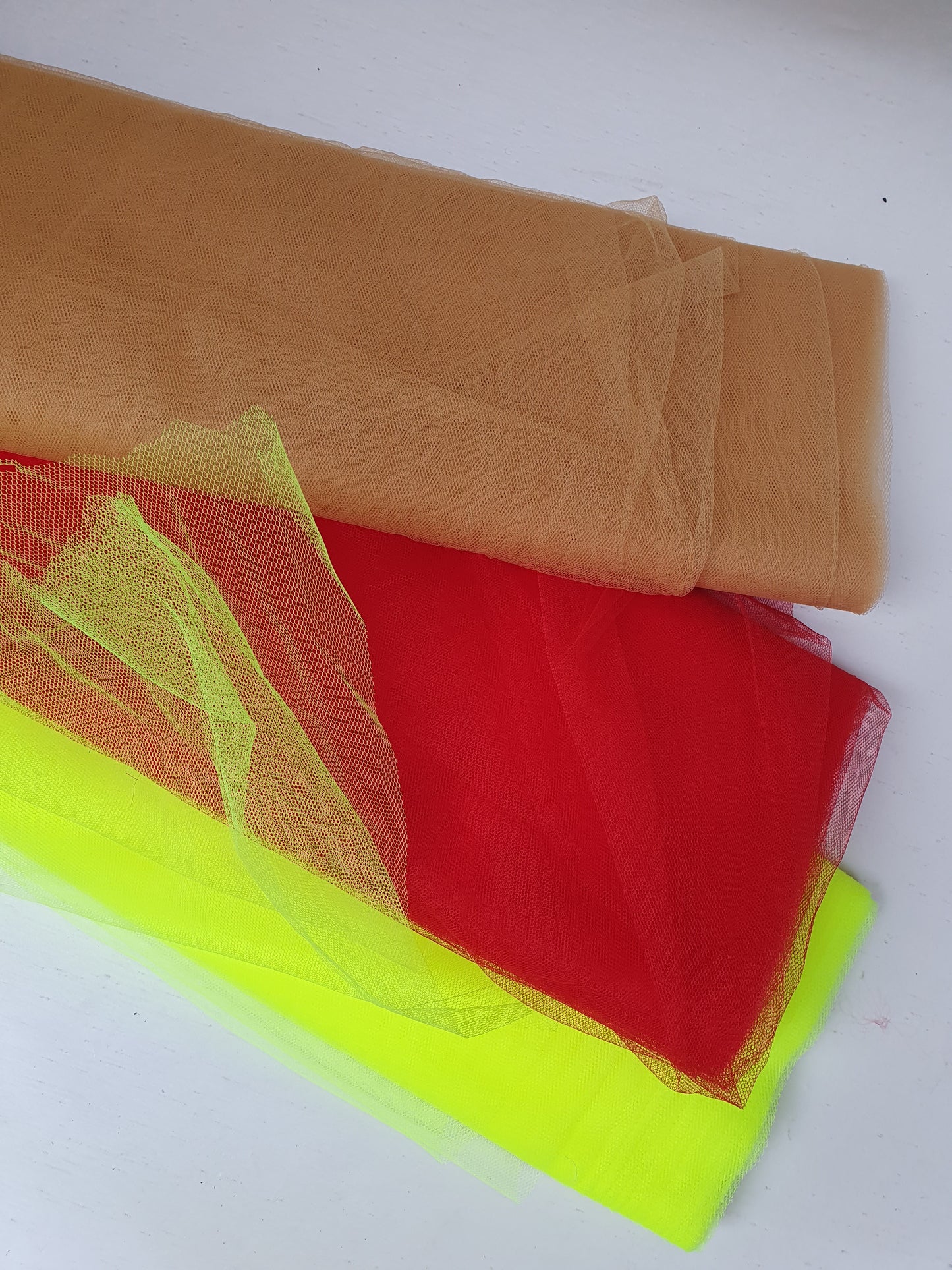 A close-up of voile tulle fabric in neon yellow, cinnamon, and red, showcasing its breathable net texture.