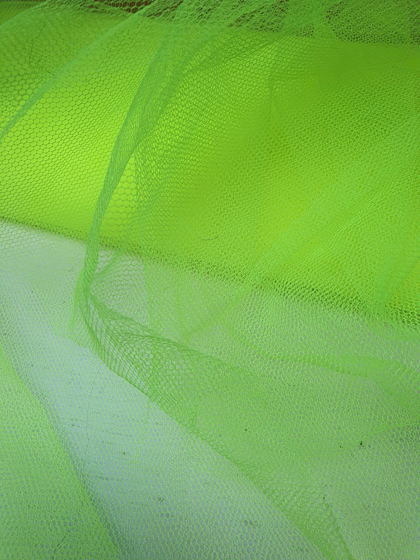 A close-up of voile tulle fabric in neon yellow, showcasing its breathable net texture.