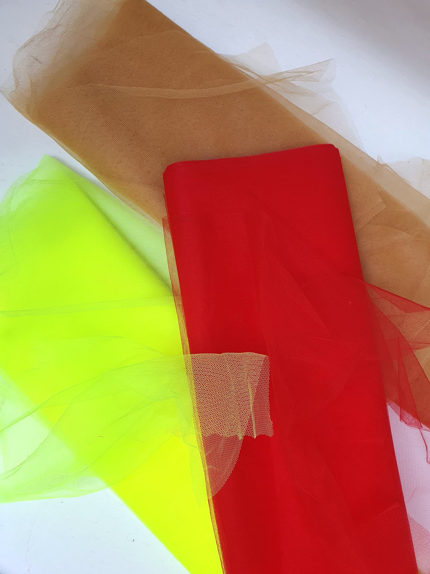 Voile tulle fabric in neon yellow, cinnamon, and red, showcasing its breathable net texture.