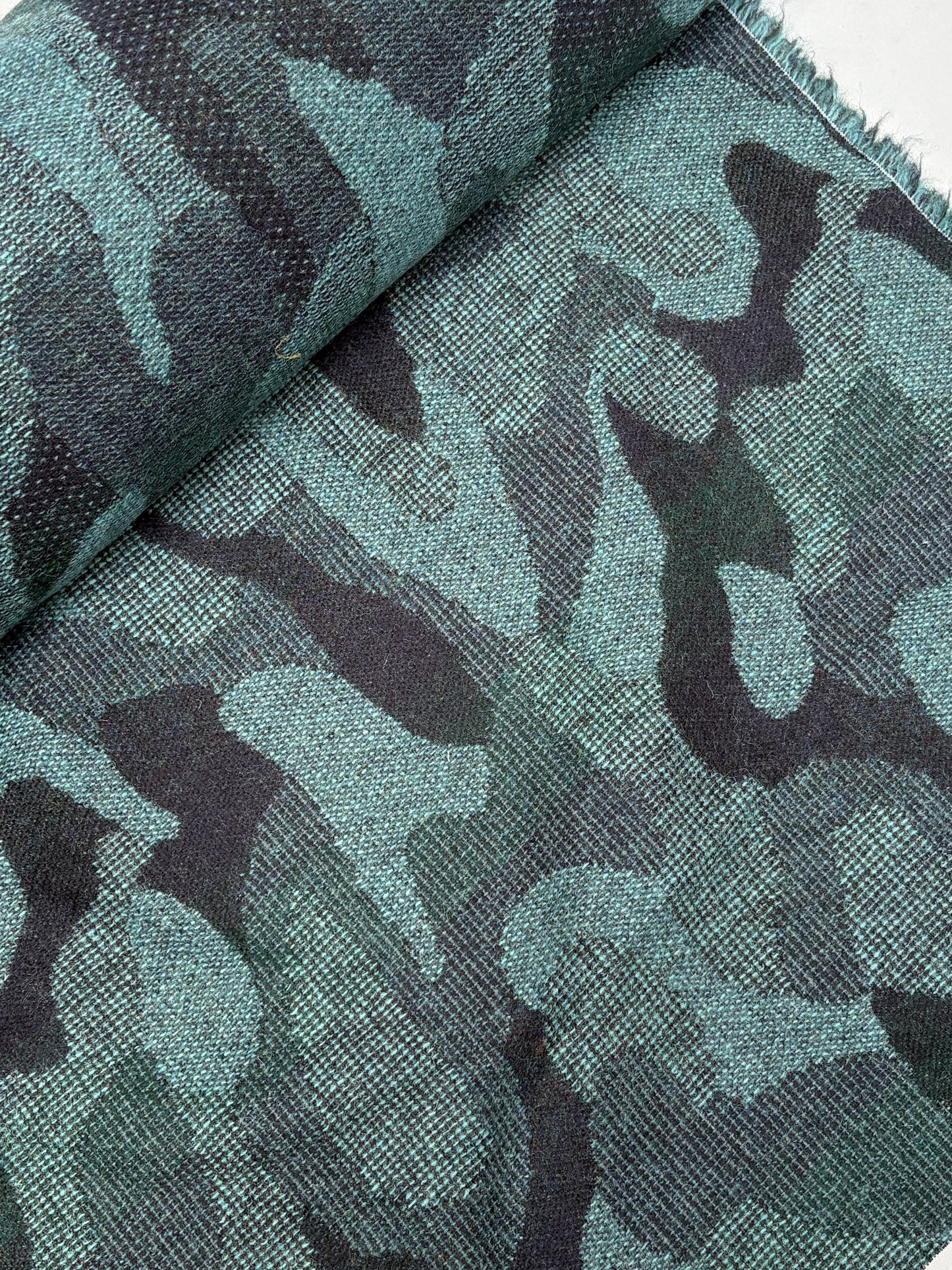 Close-up of a rolled camouflage-pattern jacquard-weave fabric in green and black.