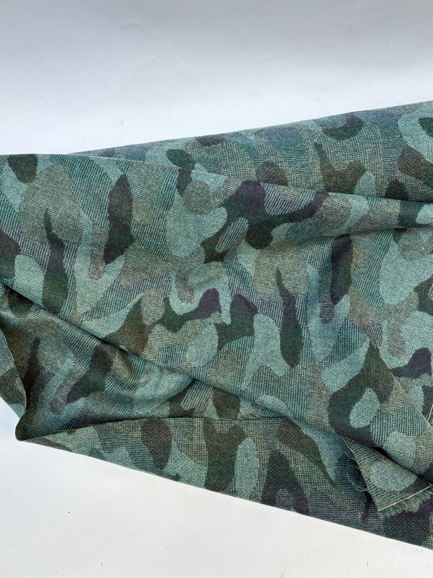 Close-up of a rolled camouflage-pattern jacquard-weave fabric in green and black.