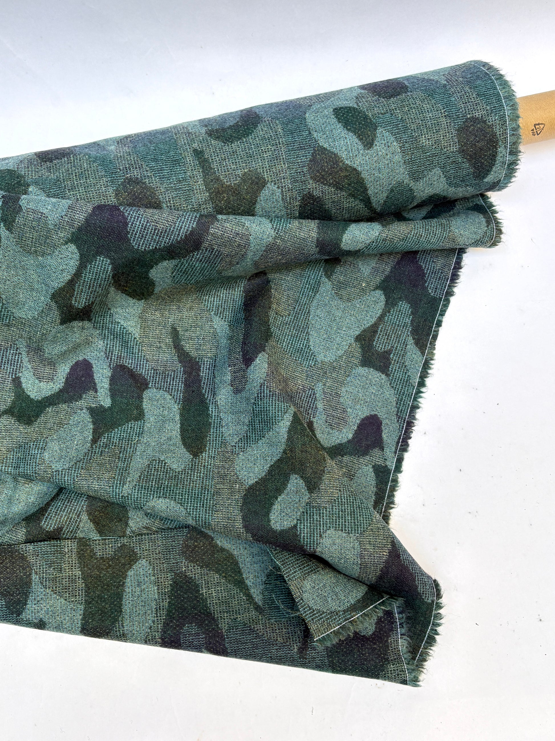 Close-up of a rolled camouflage-pattern jacquard-weave fabric in green and black with soft texture 