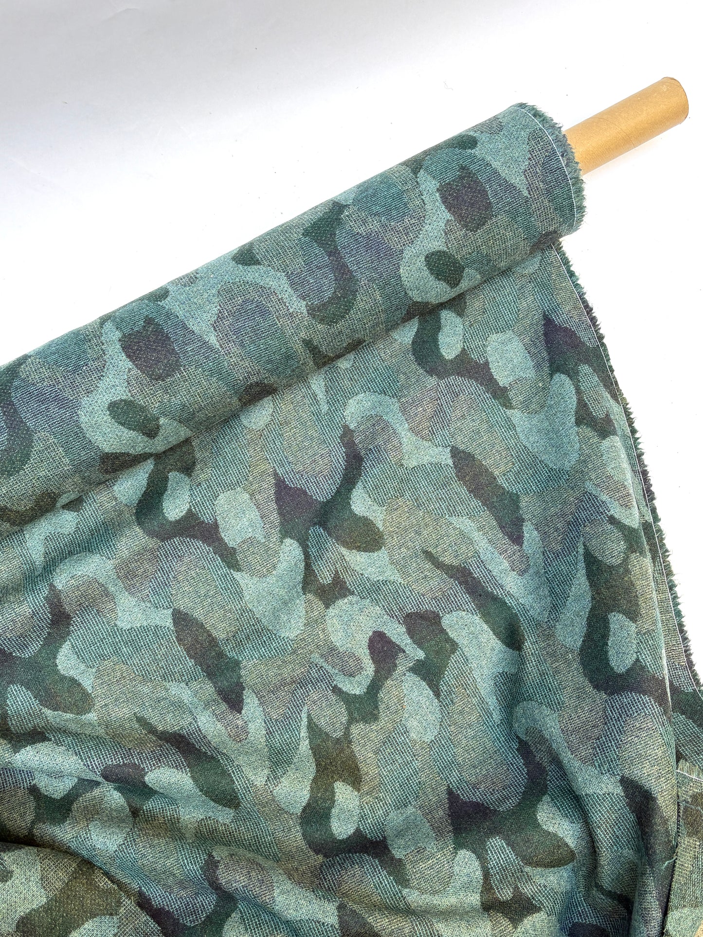 Close-up of a rolled camouflage-pattern jacquard-weave fabric in green and black with soft texture 