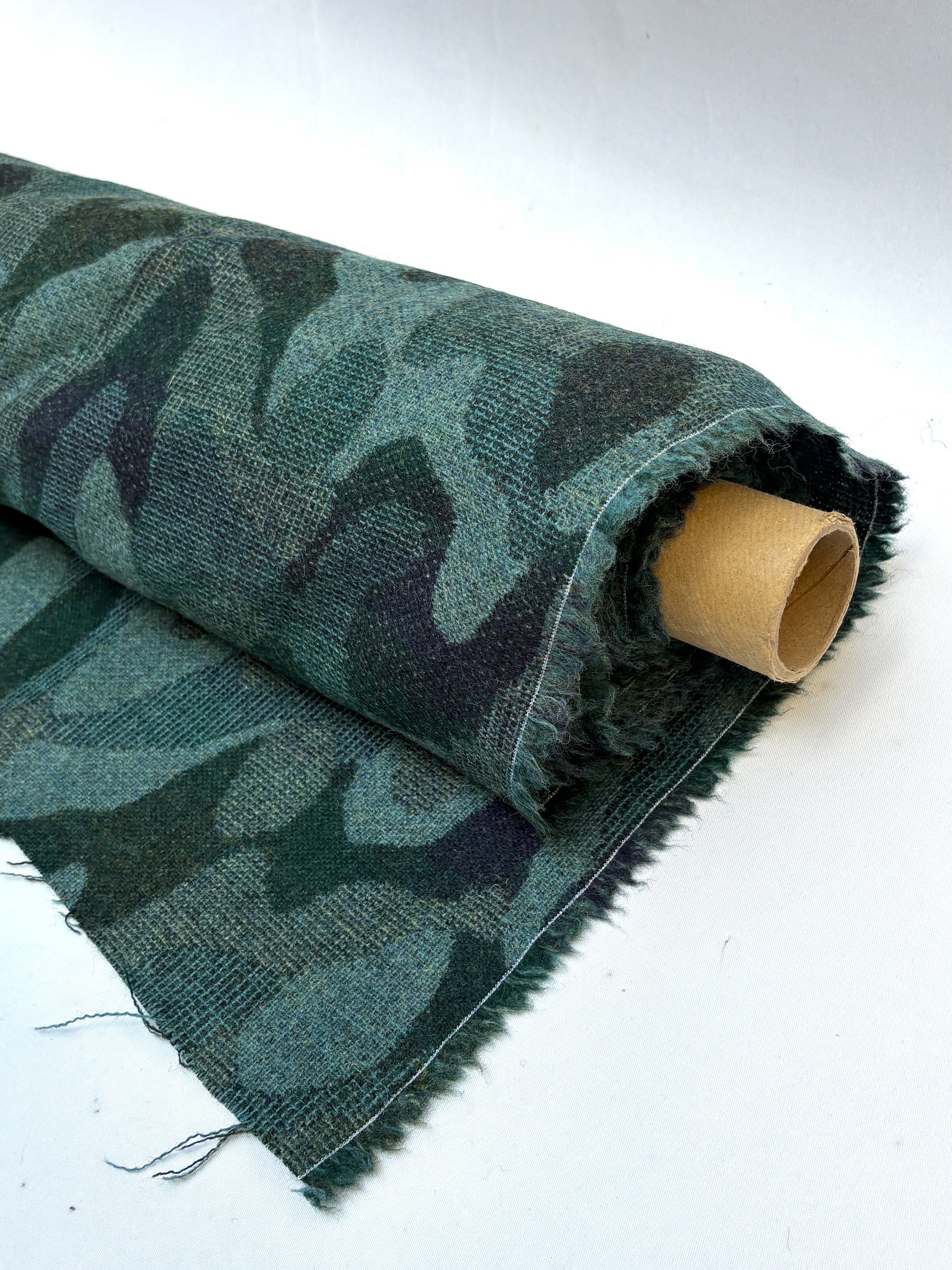 Close-up of a rolled camouflage-pattern jacquard-weave fabric in green and black with soft texture 