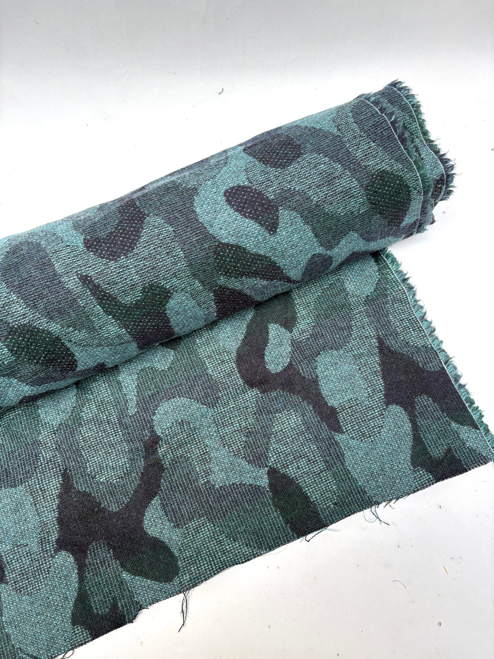 Close-up of a rolled camouflage-pattern jacquard-weave fabric in green and black with soft texture 